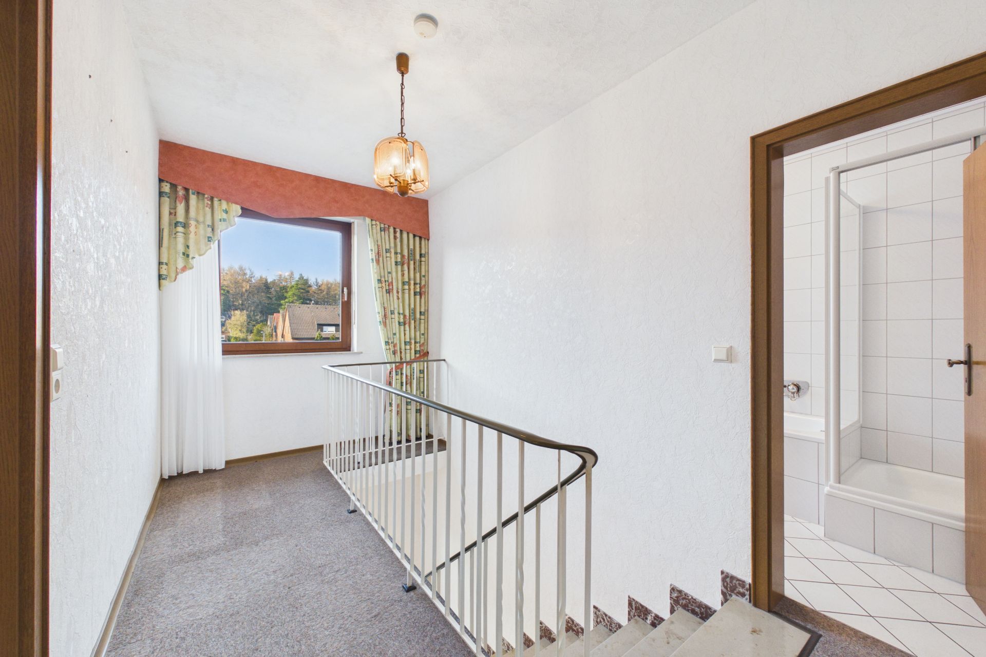 Flur mit Treppengeländer, Fenster mit Vorhang und Blick ins Badezimmer mit Badewanne.