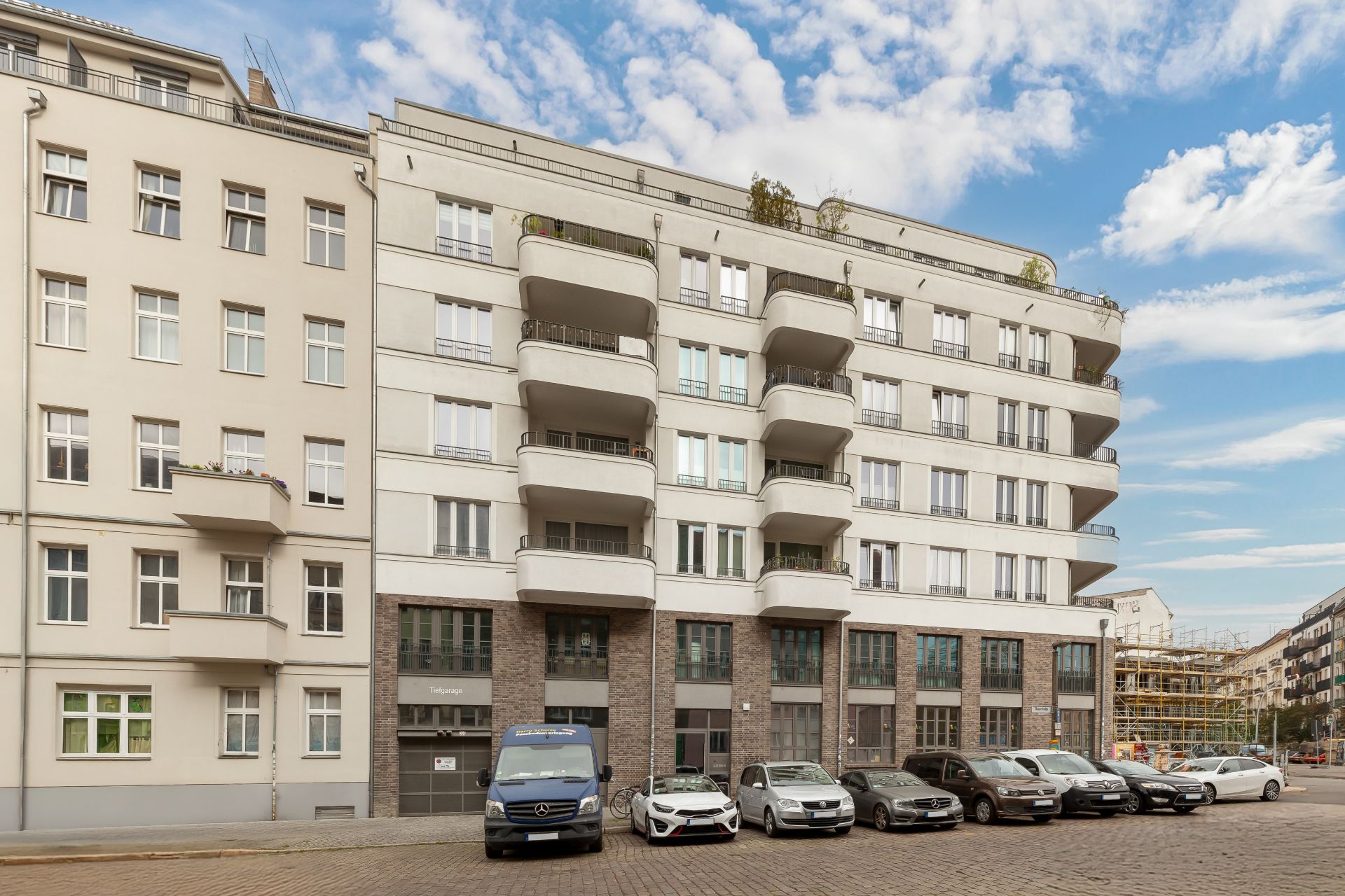 Mehrstöckiges Wohngebäude mit Balkonen und geparkten Autos davor bei Tageslicht.