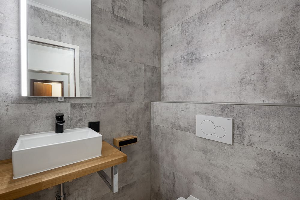 Modernes Badezimmer mit rechteckigem Waschbecken, Spiegel und grauen Fliesen.