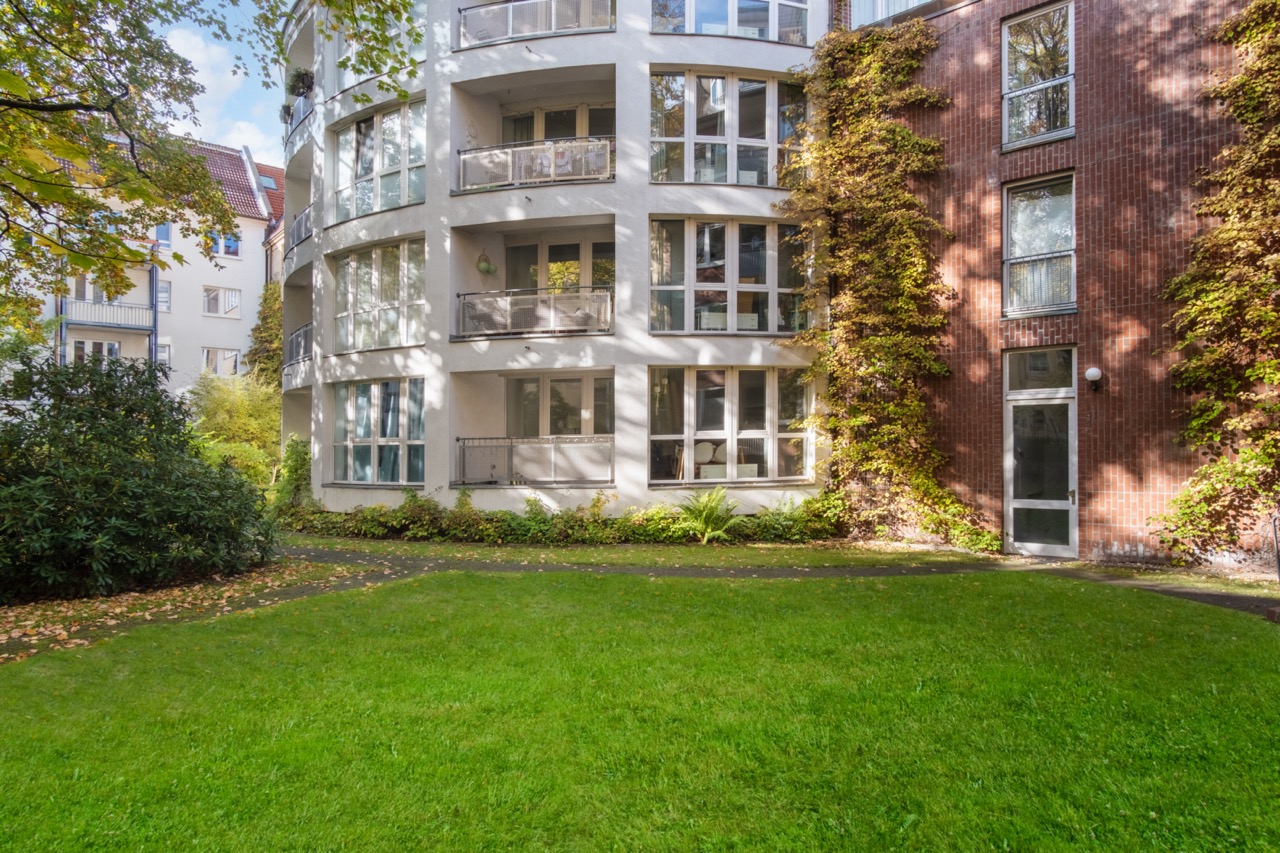 Mehrfamilienhaus mit Balkonen und großen Fenstern, davor eine Grünfläche mit Weg.