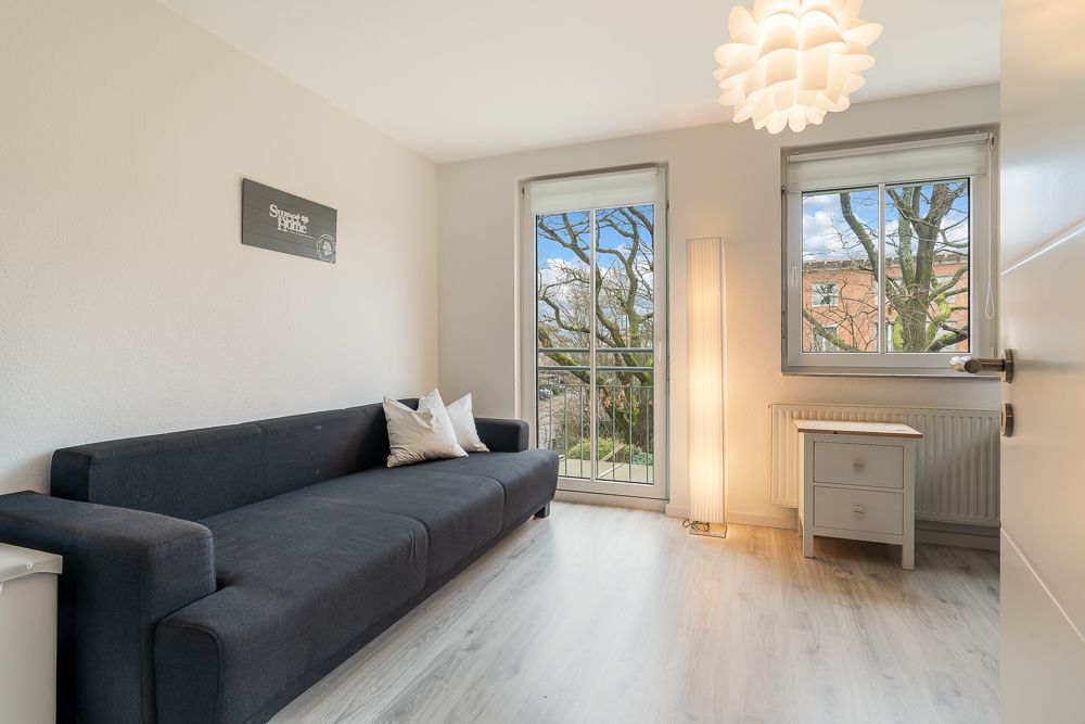 Helles Wohnzimmer mit dunkelgrauem Sofa, zwei Fenstern und weißem Beistelltisch.