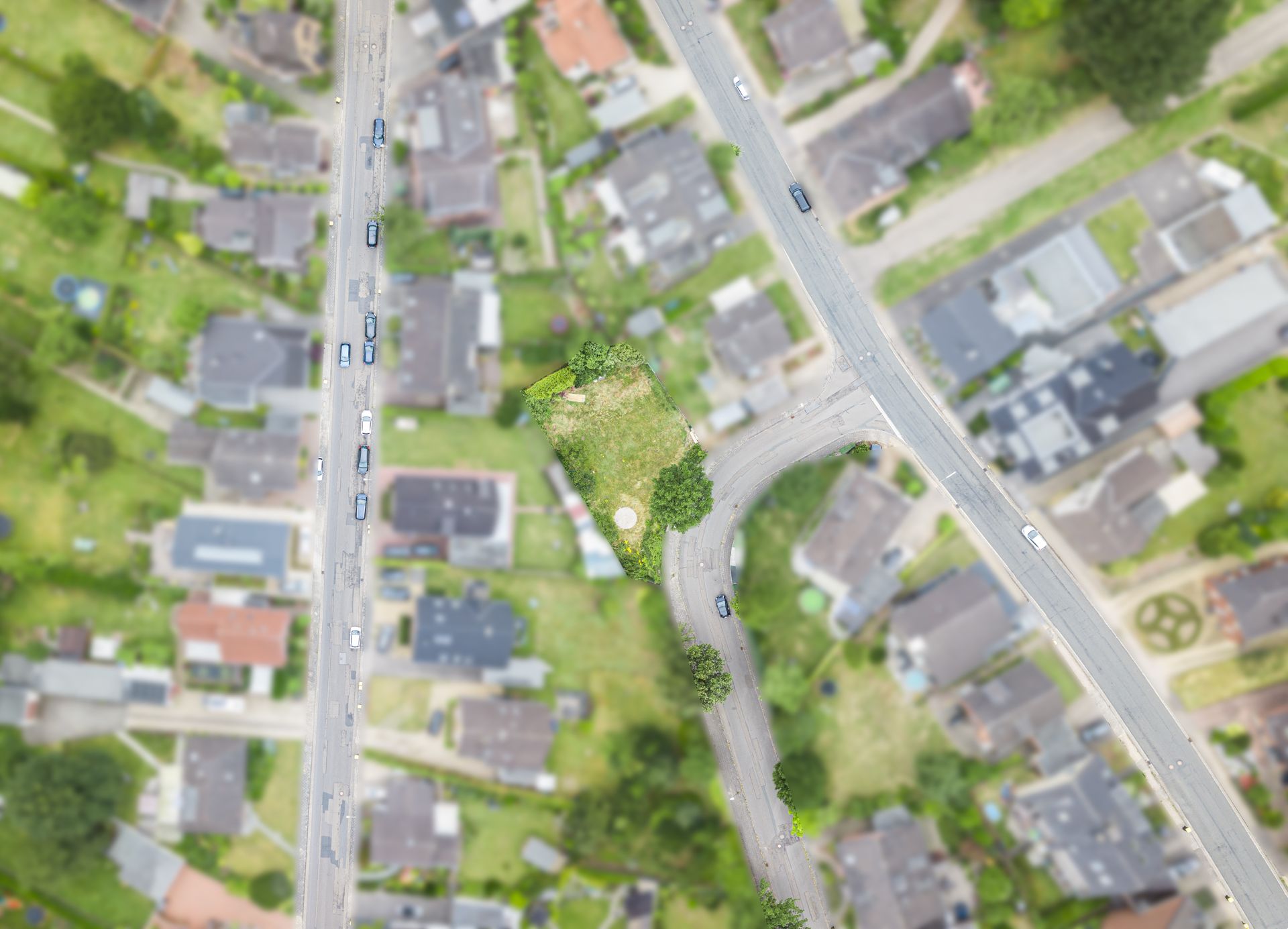 Luftaufnahme eines grünen Grundstücks an einer Straßenecke in einem Wohngebiet.