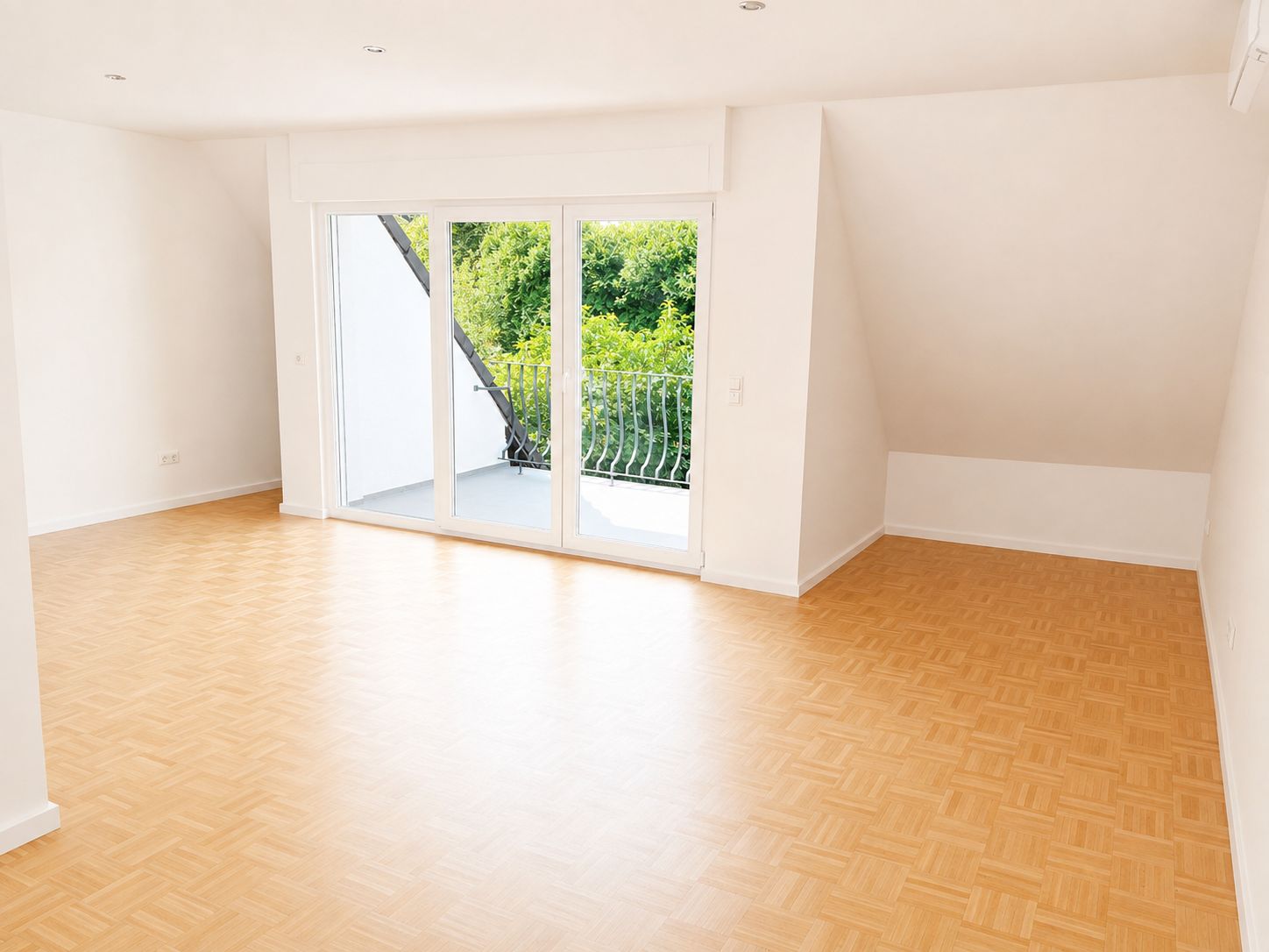 Helles, leeres Zimmer mit Parkettboden und großen Fenstern zu einem Balkon.