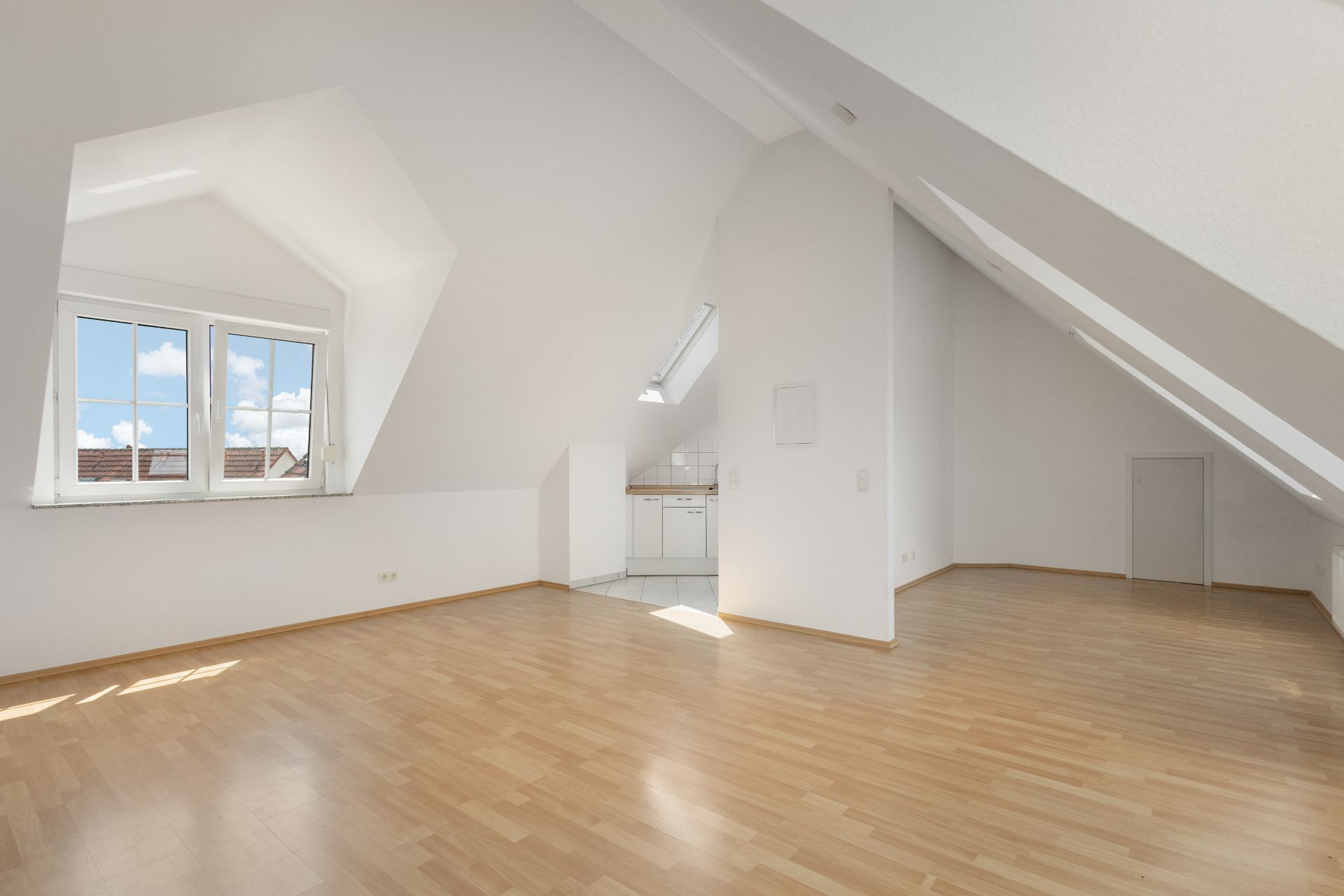 Helles Dachgeschosszimmer mit Holzfußboden, Dachfenster und kleiner Einbauküche.