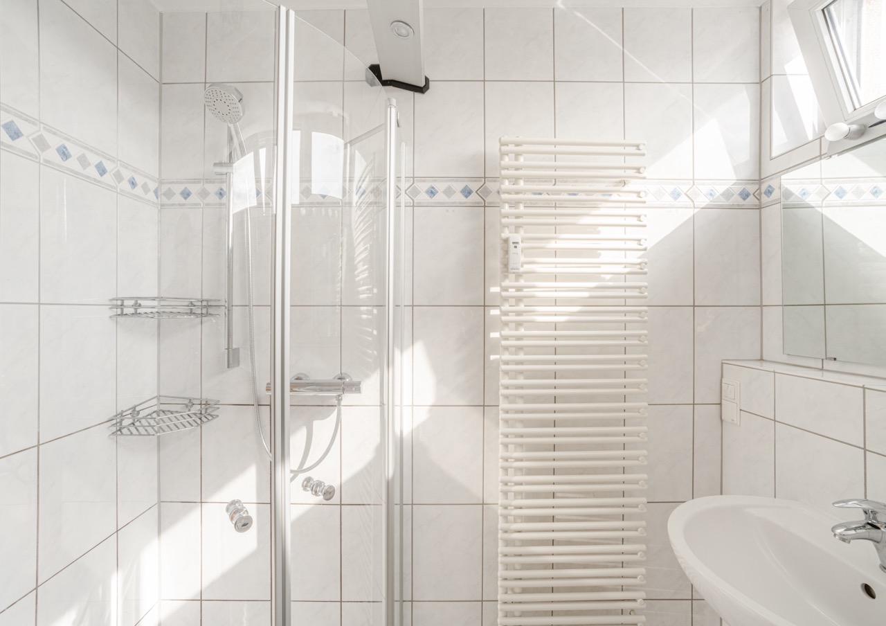 Helles Badezimmer mit Dusche, Handtuchheizung, Waschbecken und Wandspiegel.