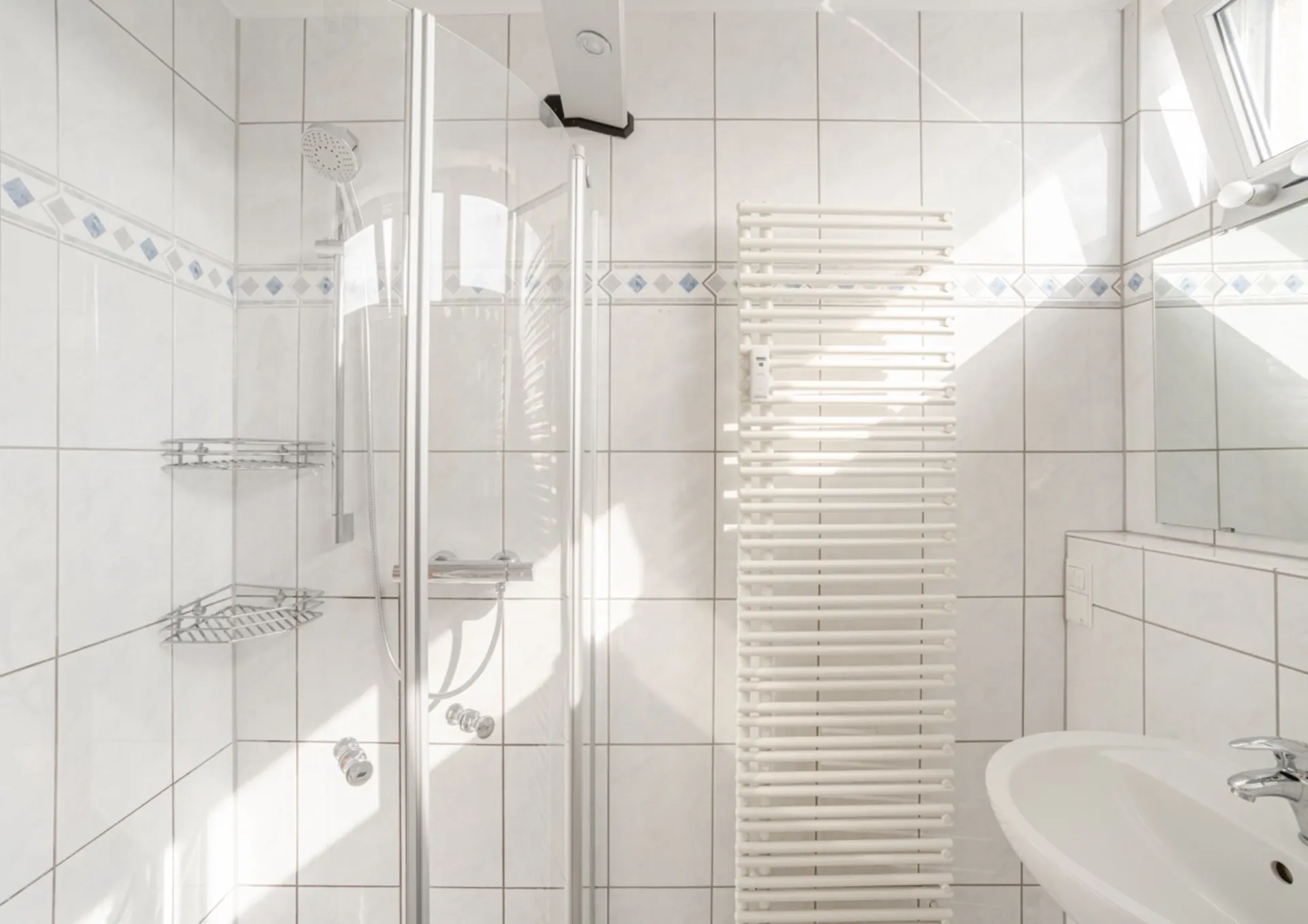 Helles Badezimmer mit Dusche, Handtuchheizung, Waschbecken und Wandspiegel.
