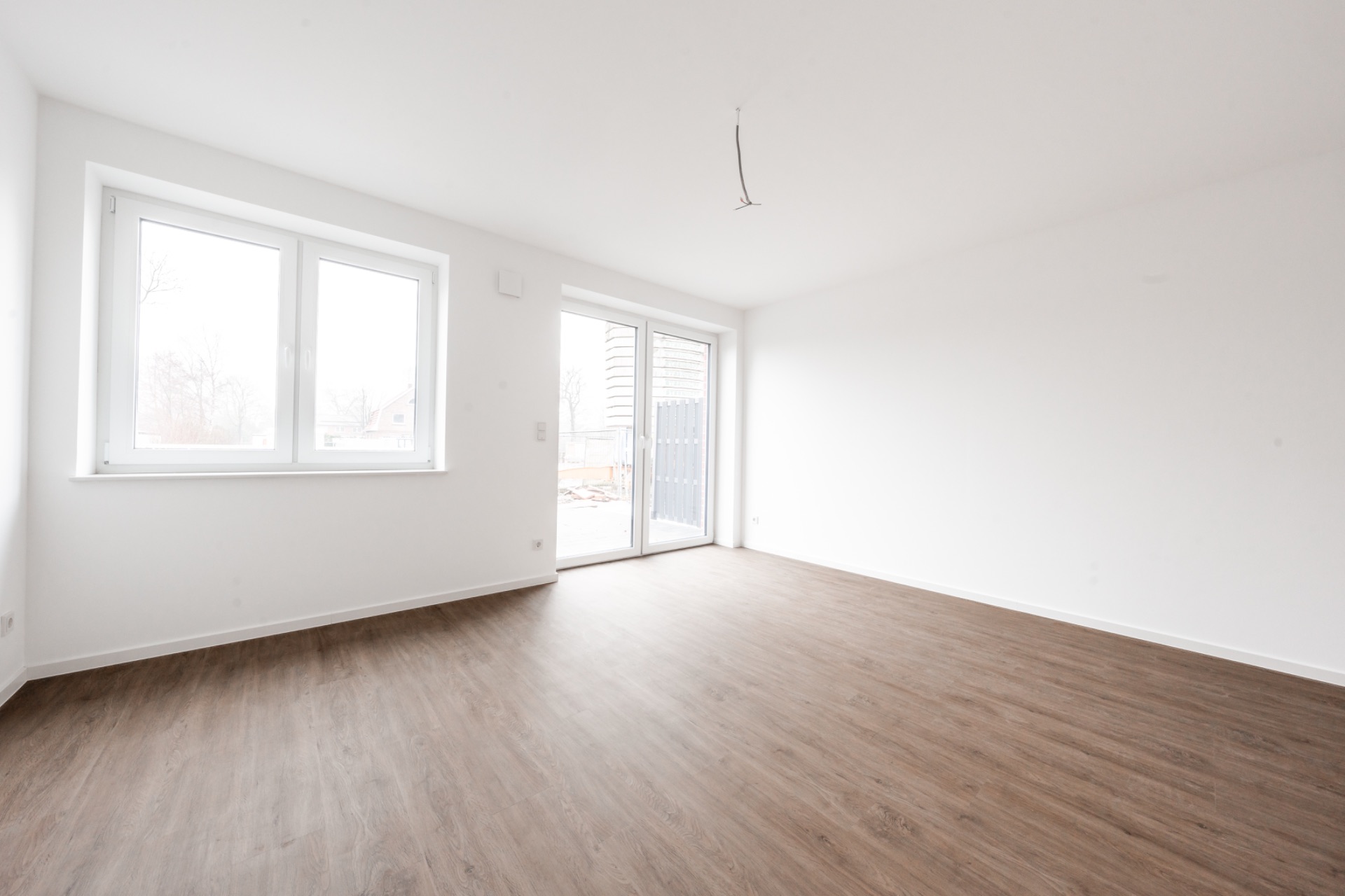 Heller, leerer Raum mit großen Fenstern und Holzfußboden.
