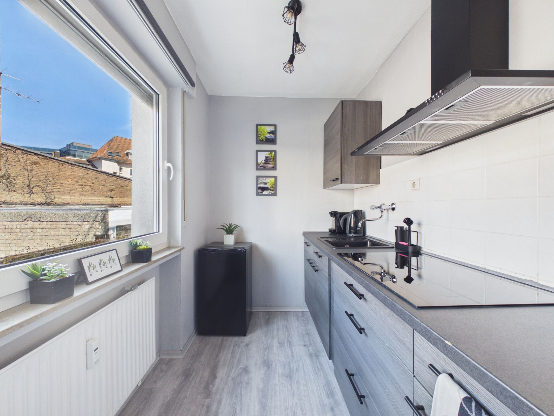 Moderne, schmale Küche mit grauen Schränken, großem Fenster und Pflanzen auf der Fensterbank.
