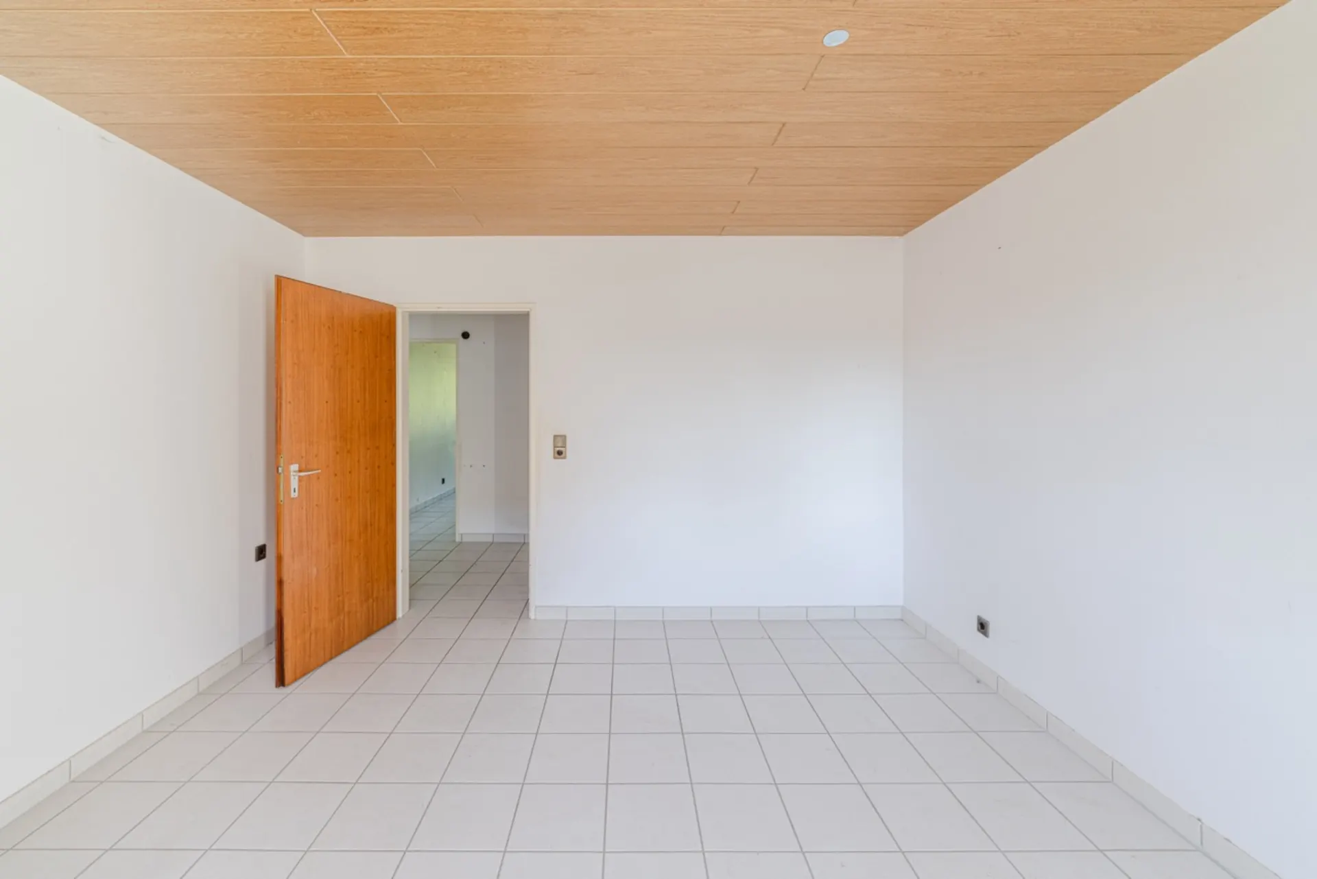 Leerer Raum mit weißen Wänden, Fliesenboden und offener Holztür.