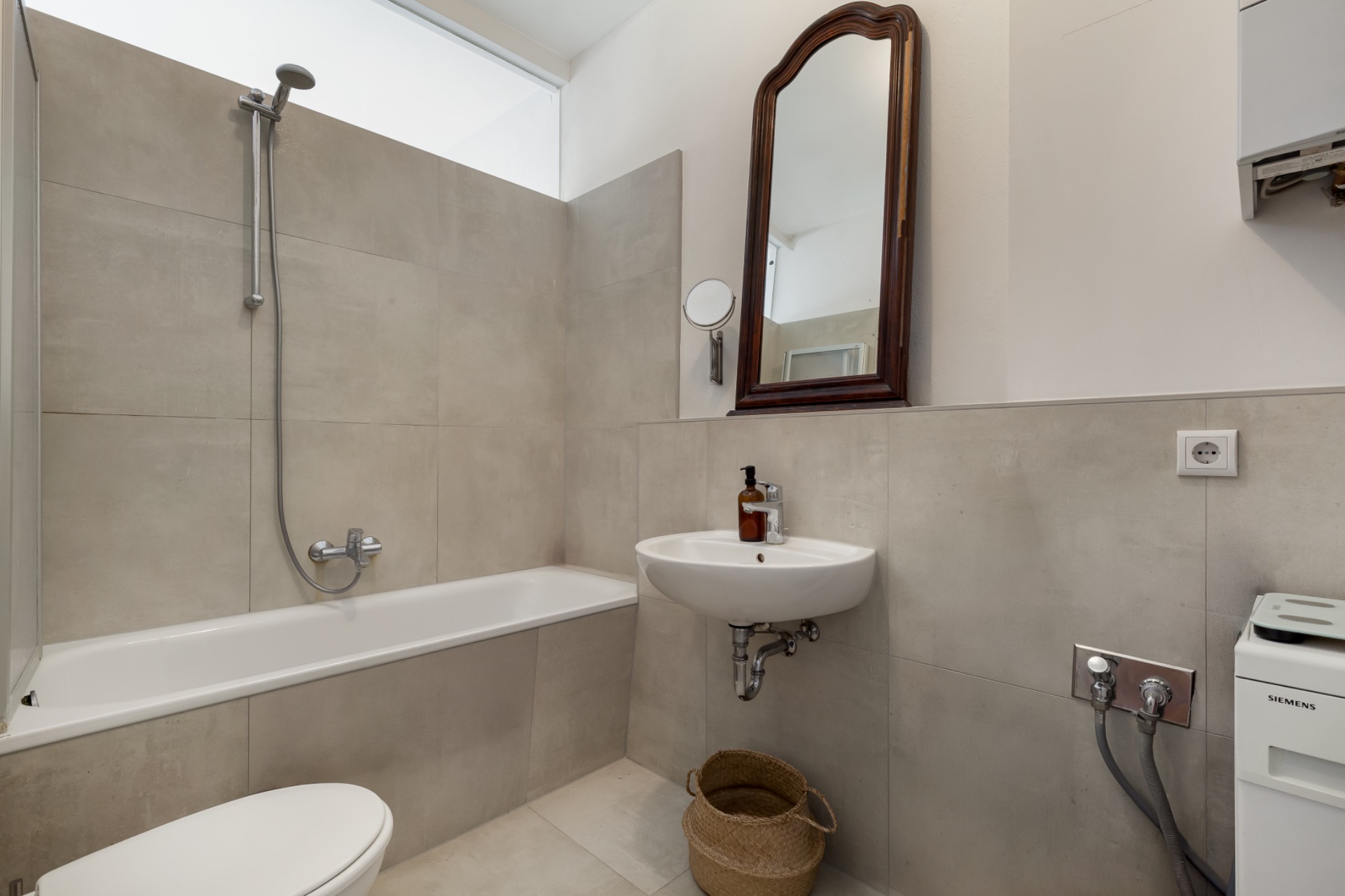 Modernes Badezimmer mit Badewanne, Waschbecken, Spiegel und Waschmaschinenanschluss.