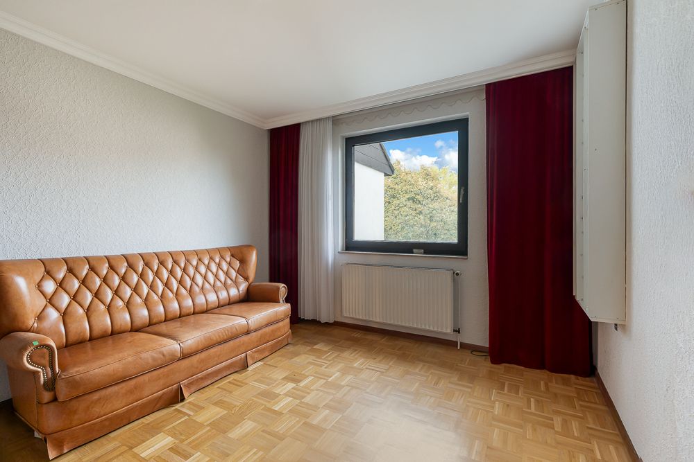 Wohnzimmer mit braunem Ledersofa, Fenster mit rotem Vorhang und Holzfußboden.