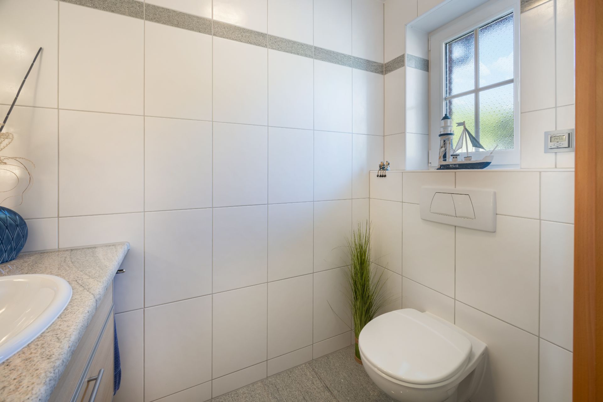 Helles Badezimmer mit Toilette, Waschbecken, Fenster und Dekoartikel auf der Fensterbank.