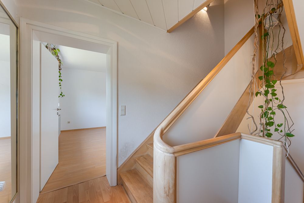 Flur mit Holztreppe, offenem Türrahmen und hängenden grünen Pflanzen an der Treppe.