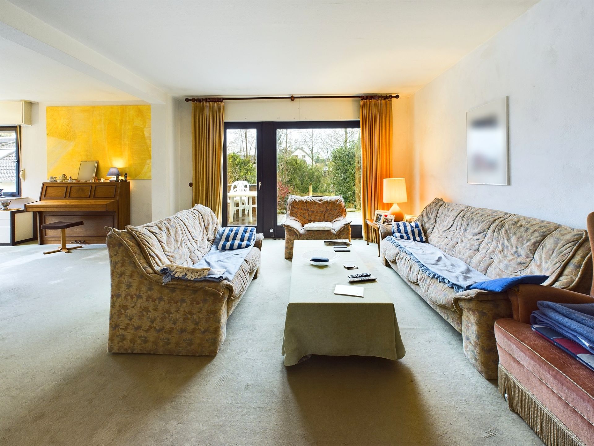 Wohnzimmer mit zwei Sofas, Sessel, Couchtisch und großen Fenstern mit Blick in den Garten.