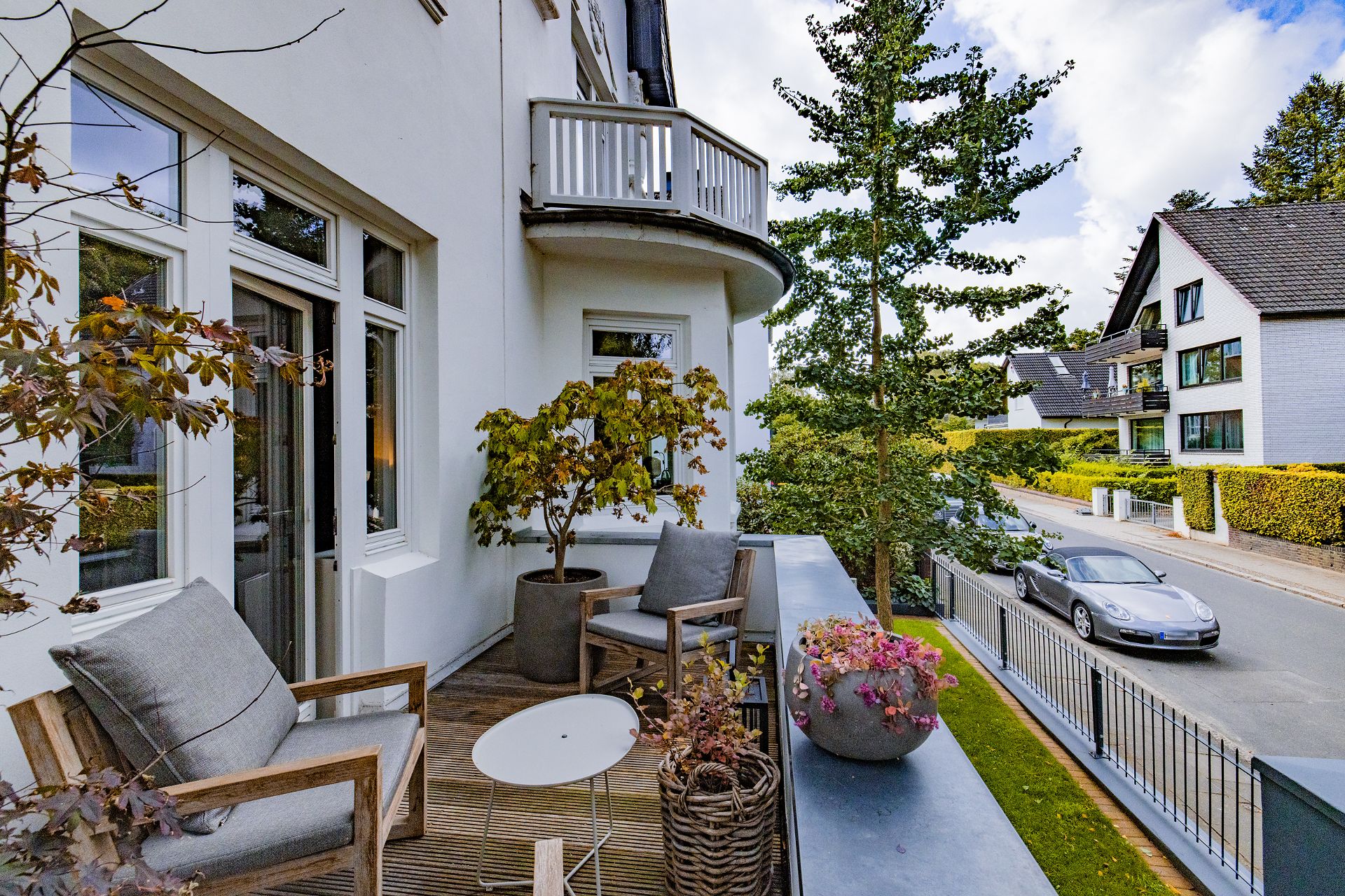 Balkon mit zwei Stühlen, Pflanzen, kleinem Tisch und Blick auf eine ruhige Wohnstraße.