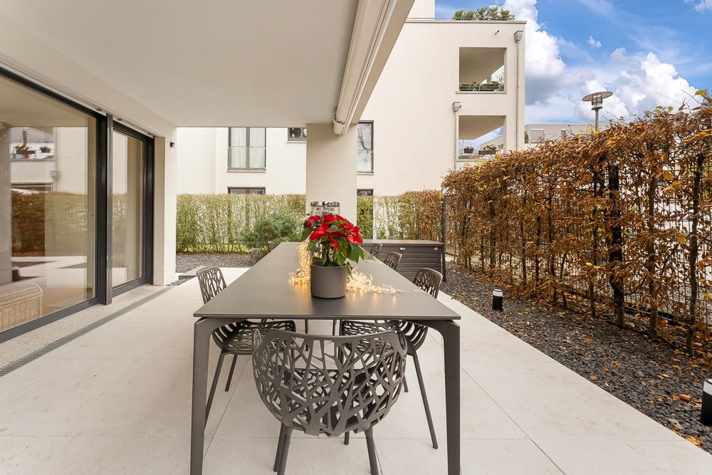 Überdachte Terrasse mit modernem Tisch, Stühlen und Pflanze in einem Wohnbereich.