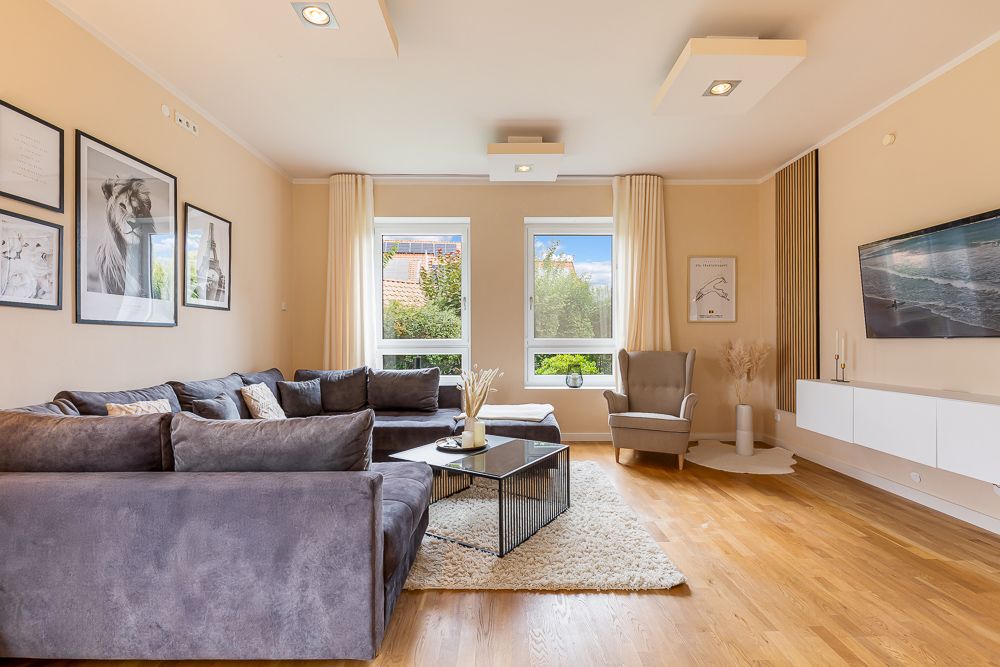 Helles Wohnzimmer mit grauem Sofa, Sessel, Couchtisch, Teppich und Wandbildern.