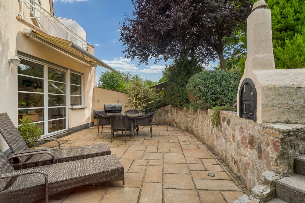 Terrasse mit Gartenmöbeln, Grill, Steinmauer und Holzofen an einem Wohnhaus.
