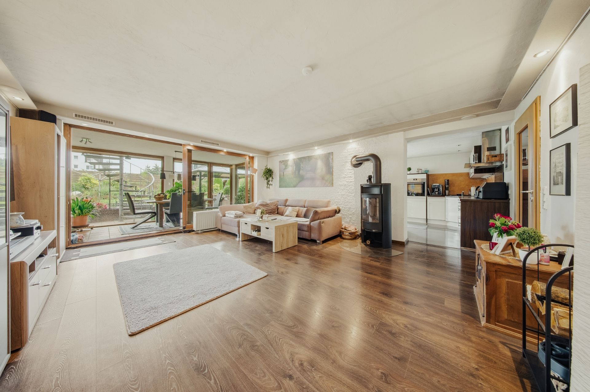 Helles Wohnzimmer mit Holzfußboden, Sofa, Kaminofen und Zugang zur Terrasse mit vielen Pflanzen.