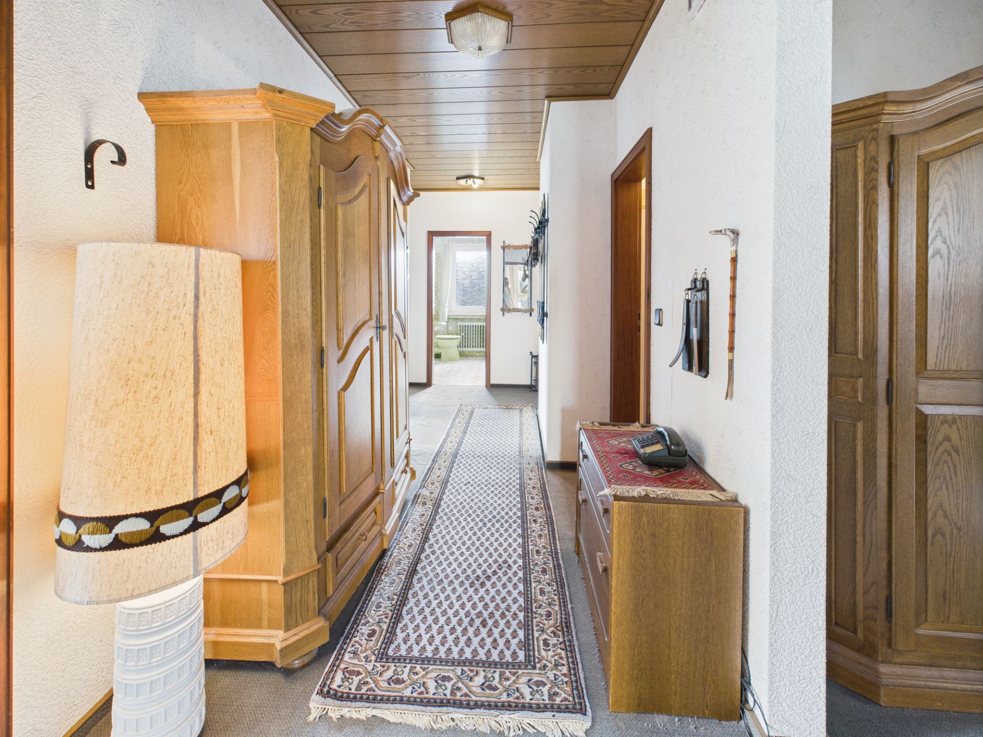Flur mit Teppichläufer, Holzschränken, Lampe und Kommode in einem Wohnhaus.