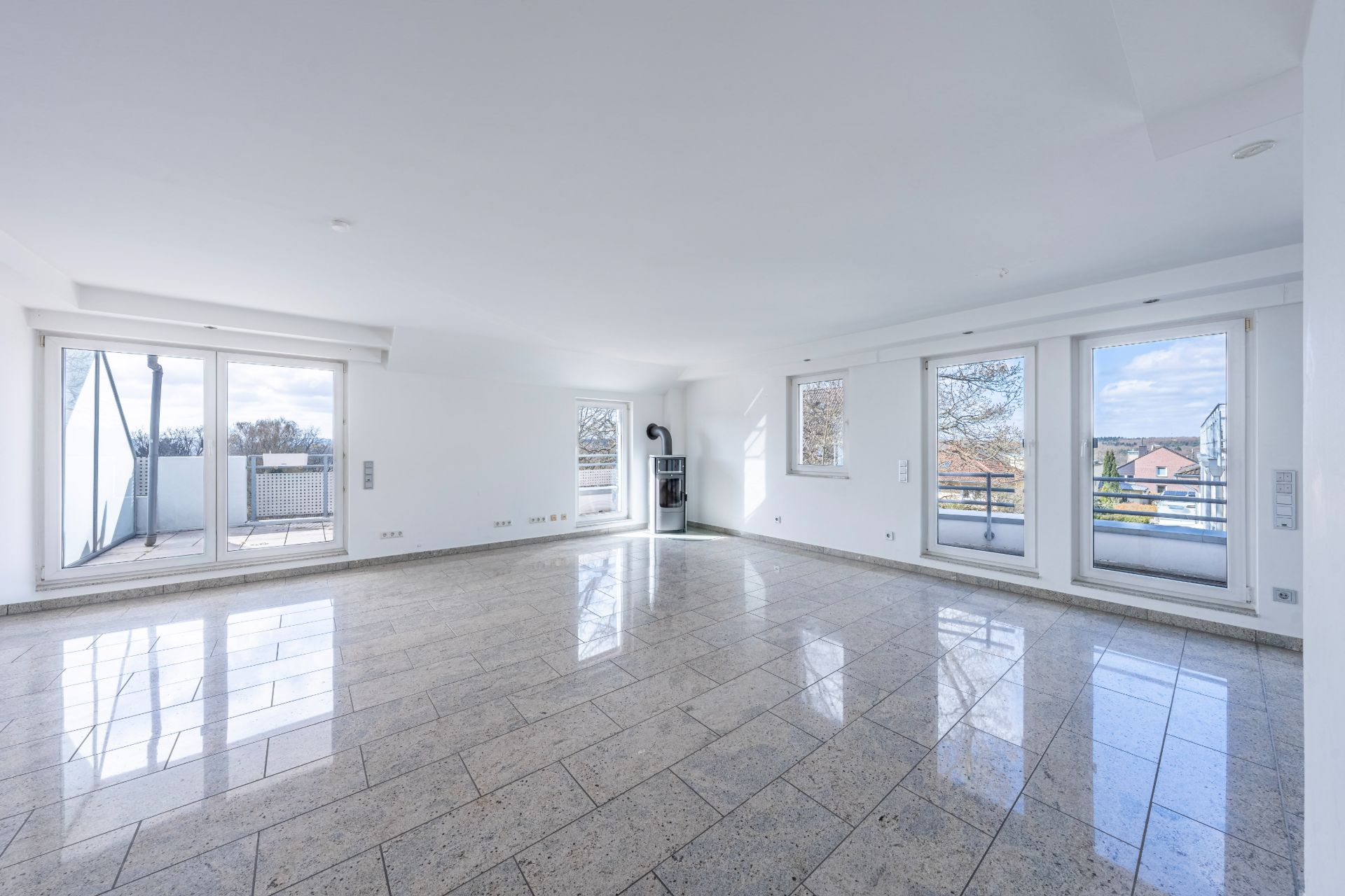 Heller, leerer Raum mit großen Fenstern und Zugang zu einem Balkon, Fliesenboden.