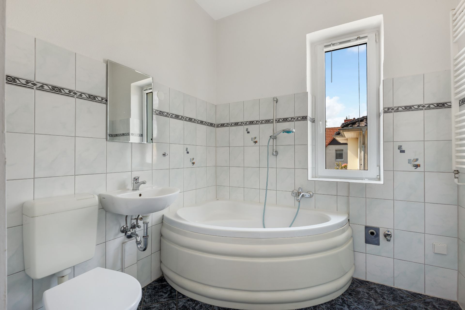 Helles Badezimmer mit Eckbadewanne, kleinem Waschbecken, WC und Fenster.