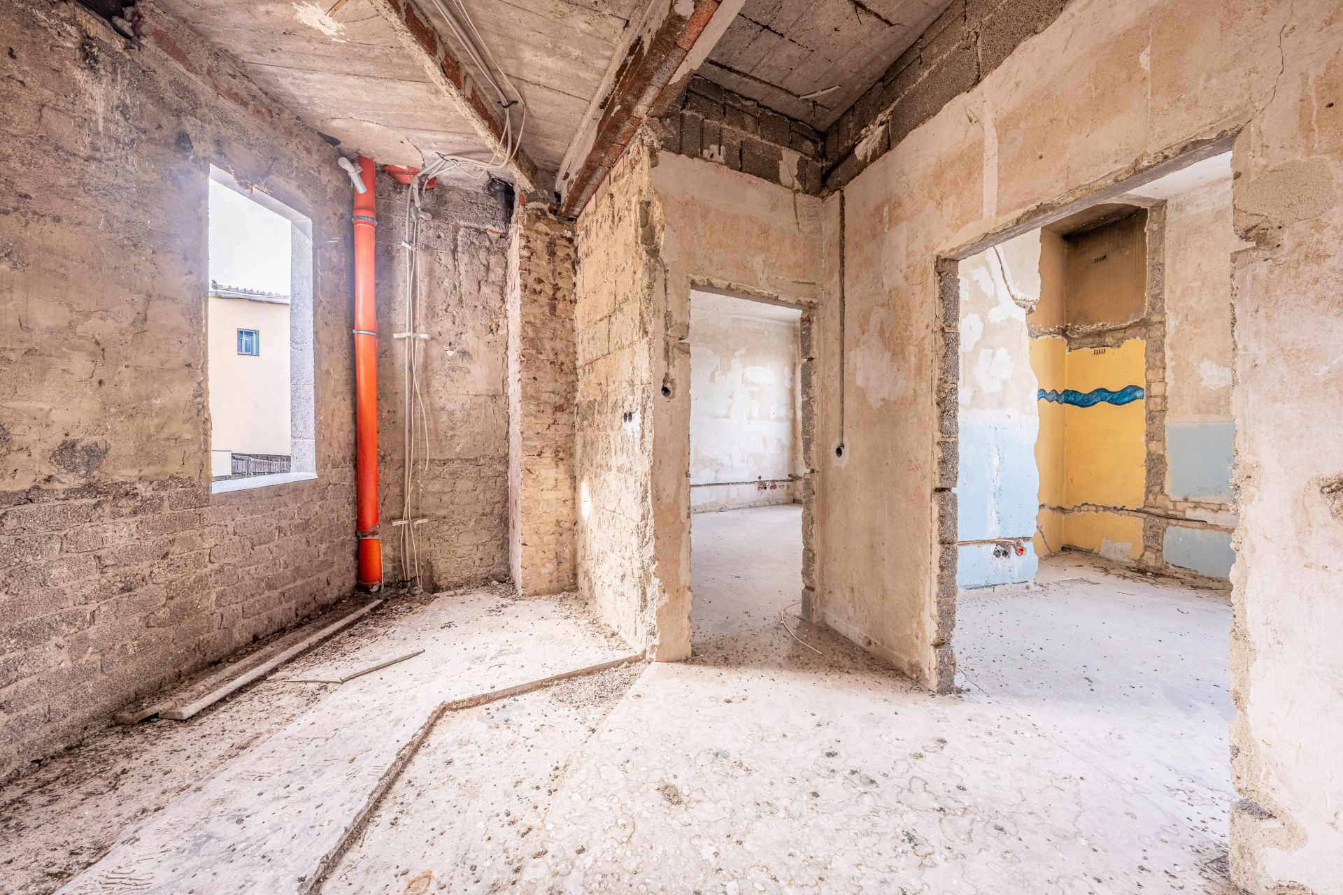 Rohbauwohnung mit offenen Wänden, sichtbaren Leitungen und Blick in mehrere Räume.