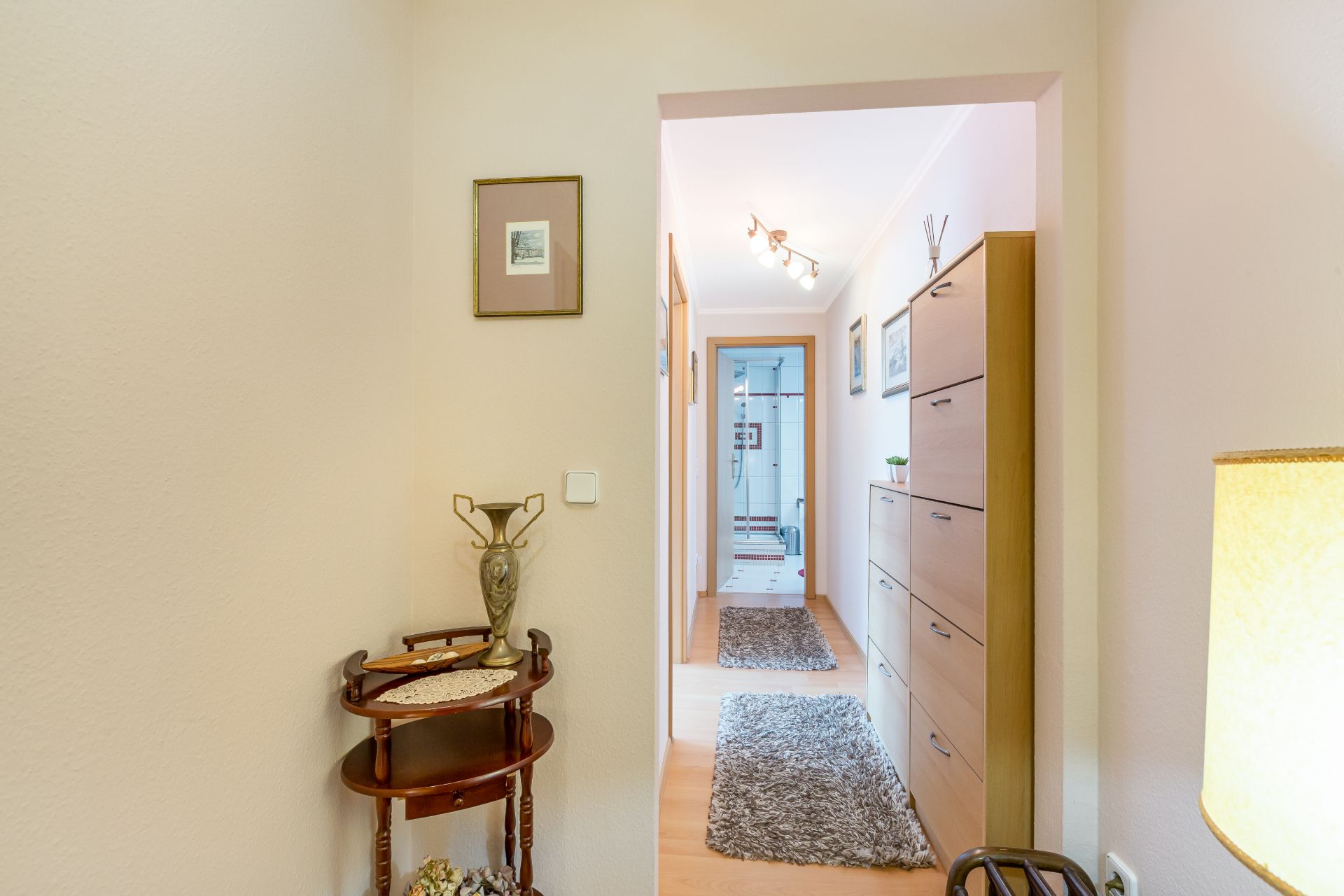 Heller Flur mit Teppichen, Sideboard, kleinem Tisch und Wandbildern in einer Wohnung.