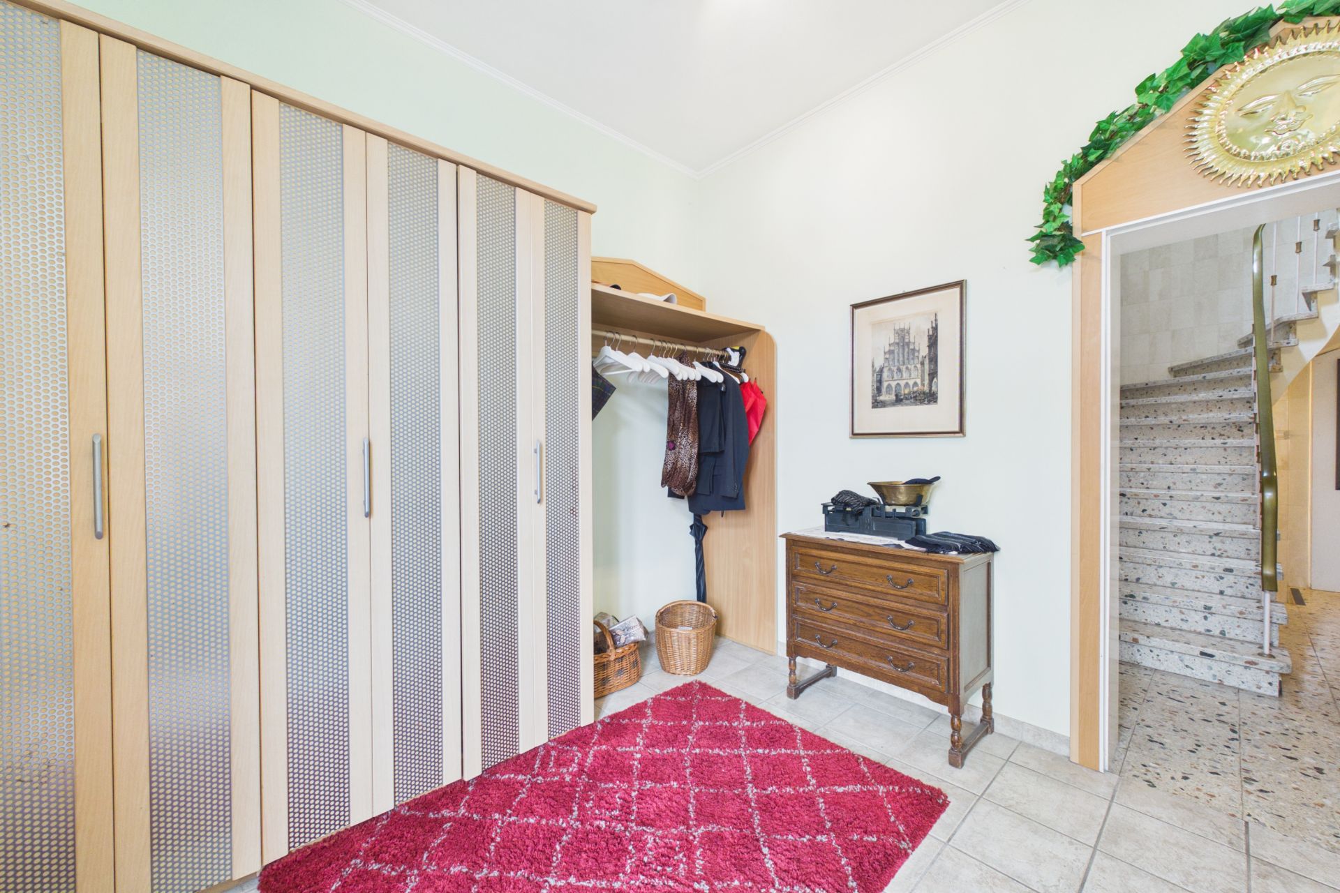Flur mit großem Schrank, rotem Teppich, Kommode, Garderobe und Treppe im Hintergrund.
