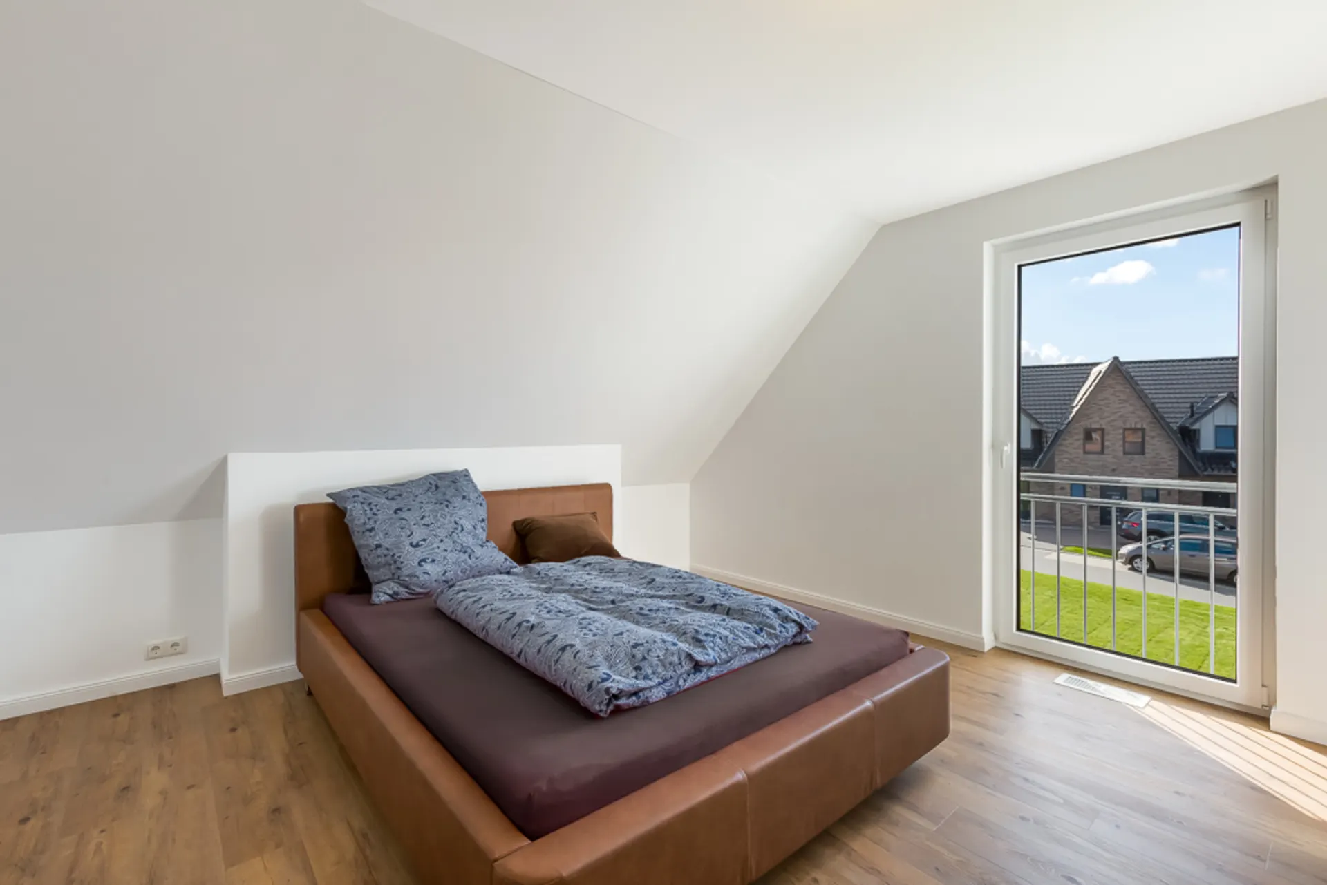 Schlafzimmer mit braunem Bett, Holzboden und großem Fenster mit Blick nach draußen.