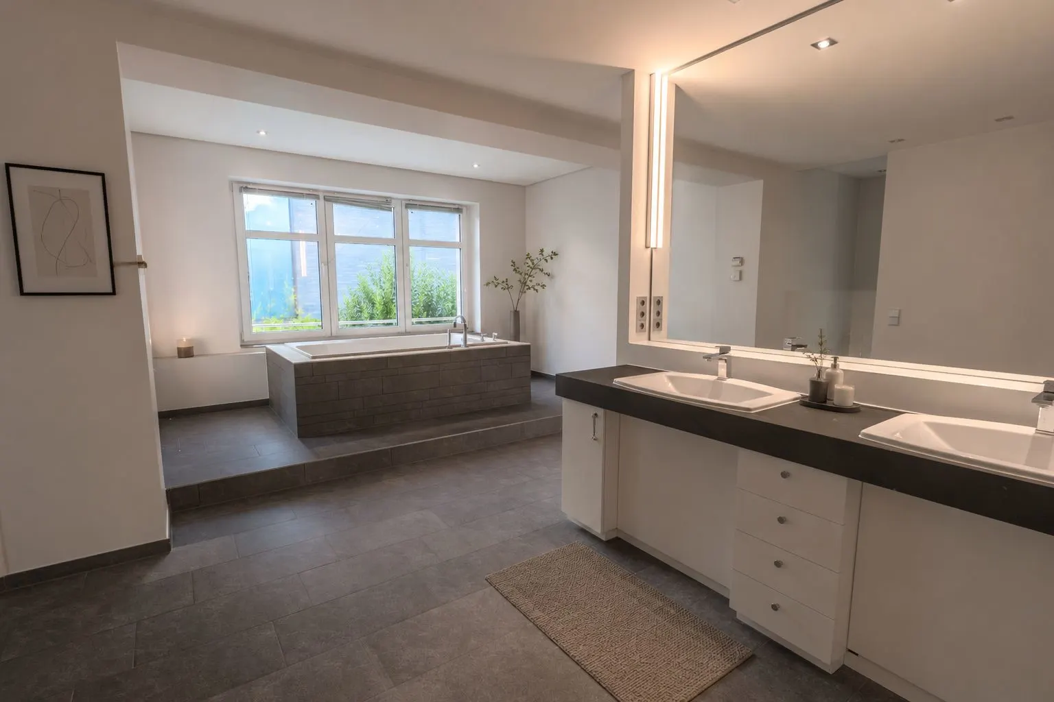 Modernes Badezimmer mit großer Badewanne und zwei Waschbecken, Fenster mit Ausblick und schlichter Dekoration.