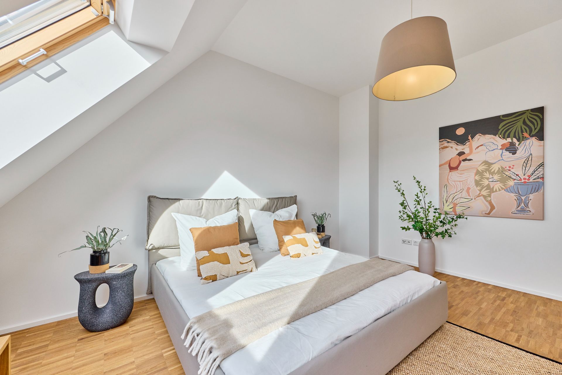 Helles Schlafzimmer mit Doppelbett, Dachfenster, Pflanzen und Wandbild auf Holzboden.