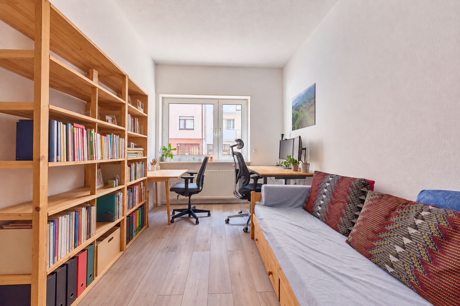 Helles Arbeitszimmer mit Bücherregal, Schreibtischen, Stühlen und einem Sofa.