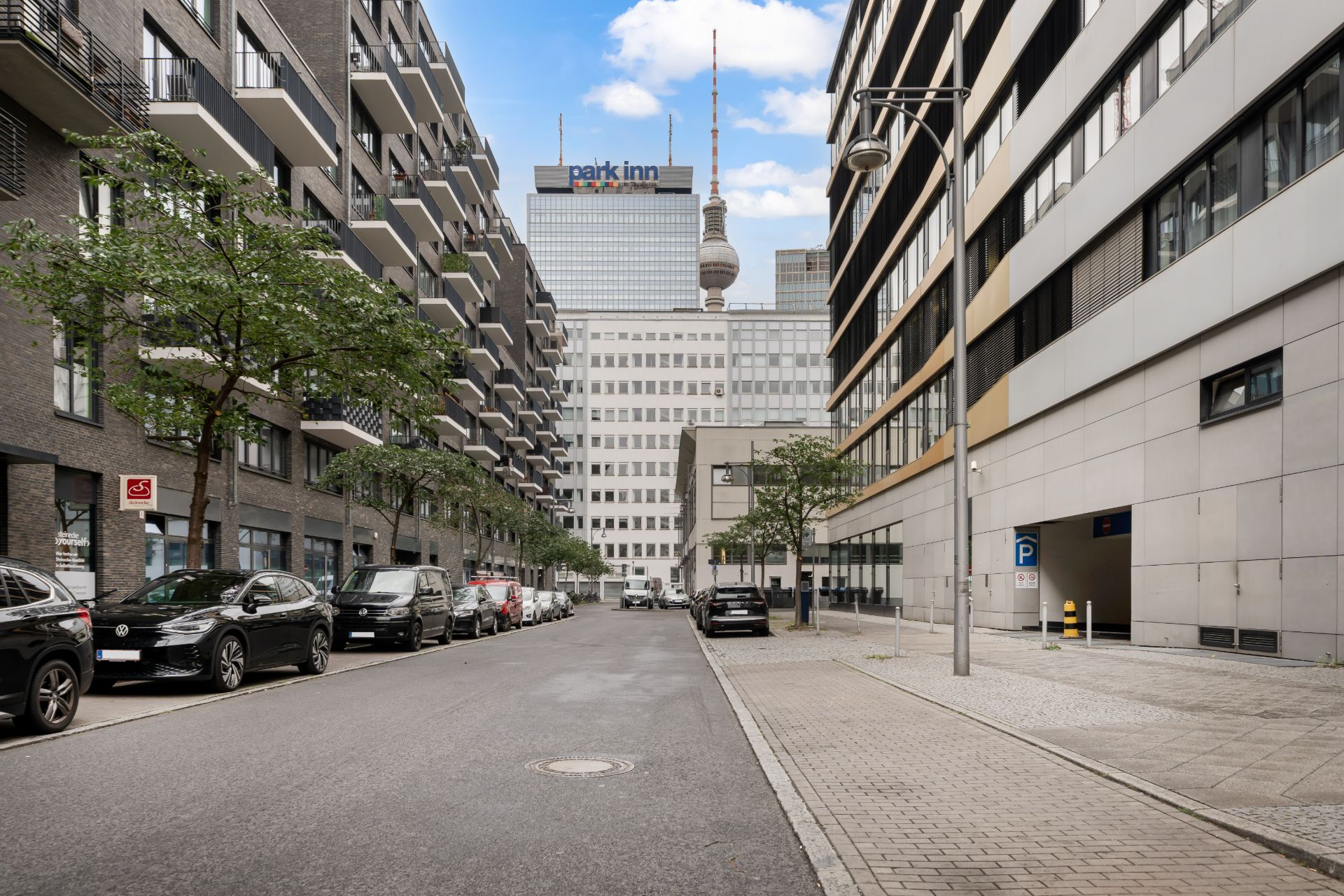 Moderne Wohngebäude an einer ruhigen Straße mit geparkten Autos und Bäumen.