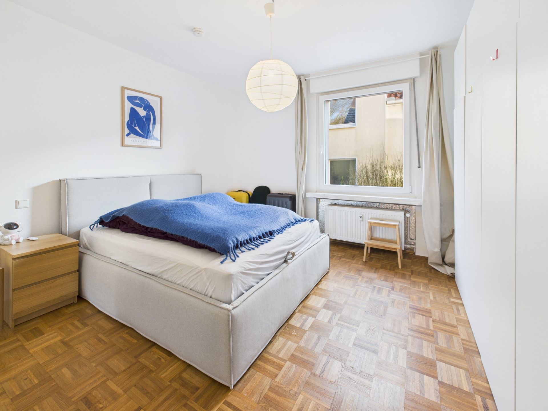 Helles Schlafzimmer mit Doppelbett, Nachttisch, Fenster und Kleiderschrank.