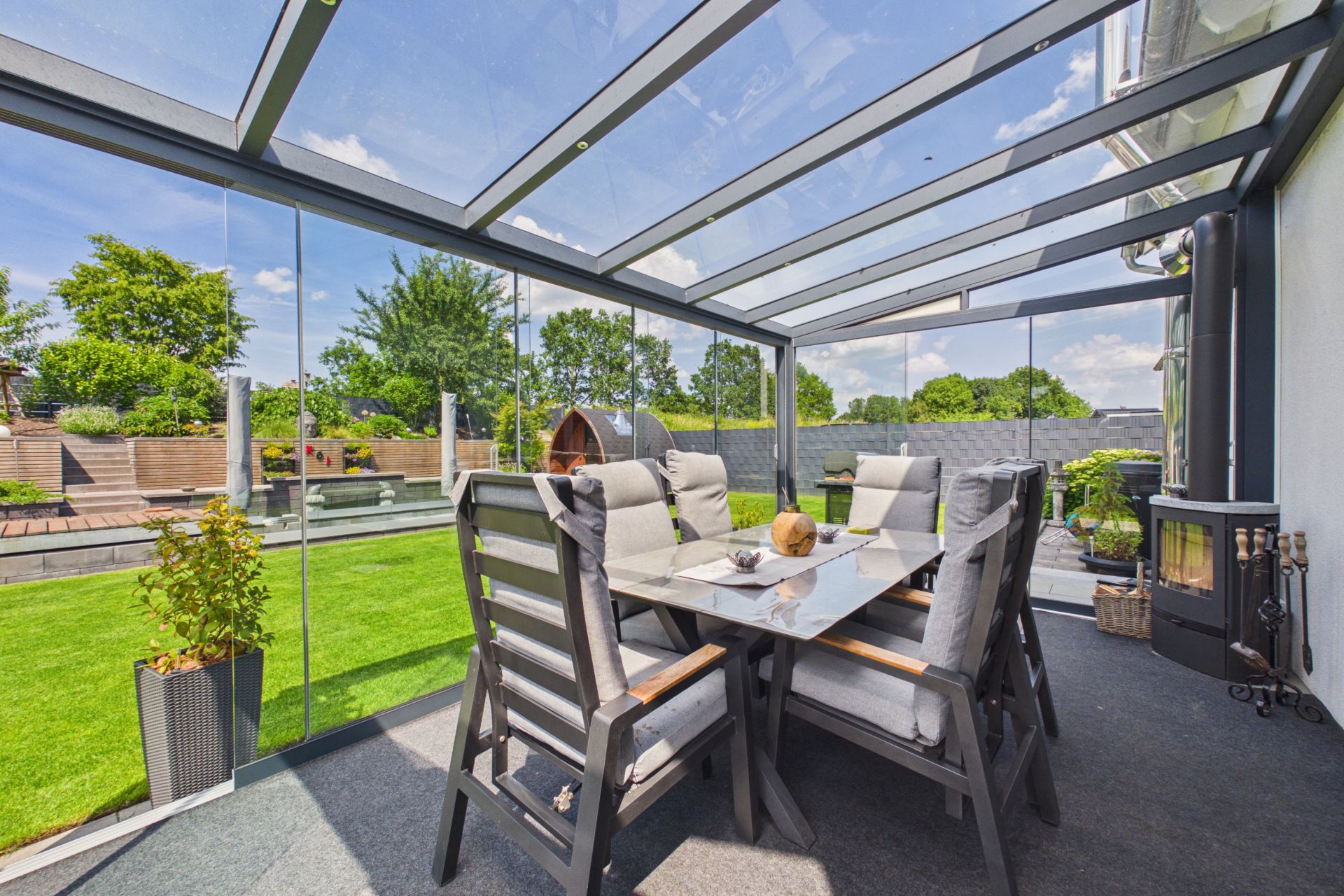 Überdachte Terrasse mit Glastisch, sechs Stühlen und Blick auf einen grünen Garten.