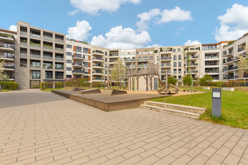 Wohnanlage mit Spielplatz im Innenhof, umgeben von modernen mehrstöckigen Gebäuden.