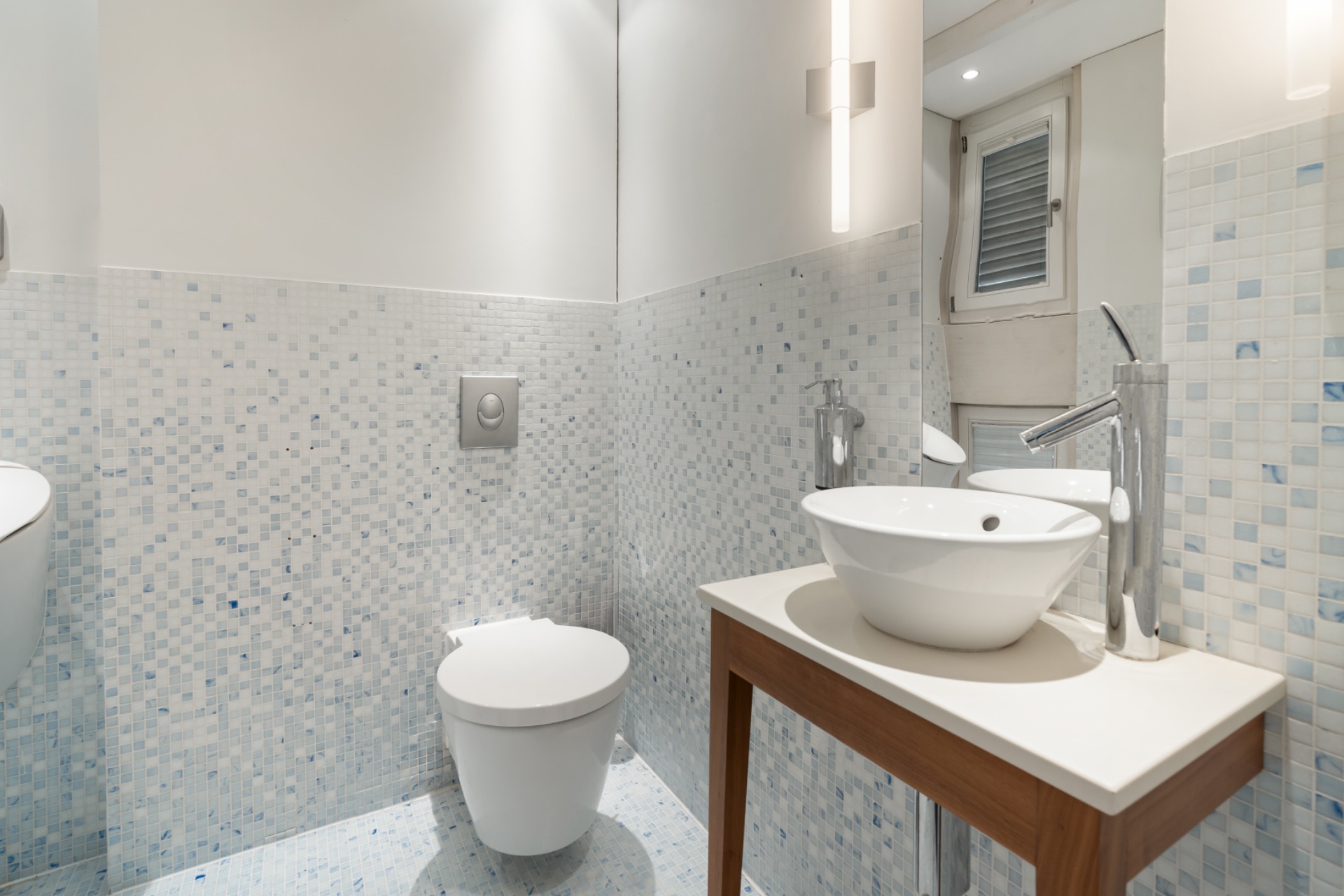 Modernes Badezimmer mit Wandtoilette, Waschbecken auf Holzgestell und Mosaikfliesen.