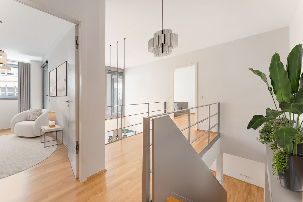 Heller Flur mit Treppe, Holzfußboden, Zimmerpflanze und Sitzbereich rechts im Bild.