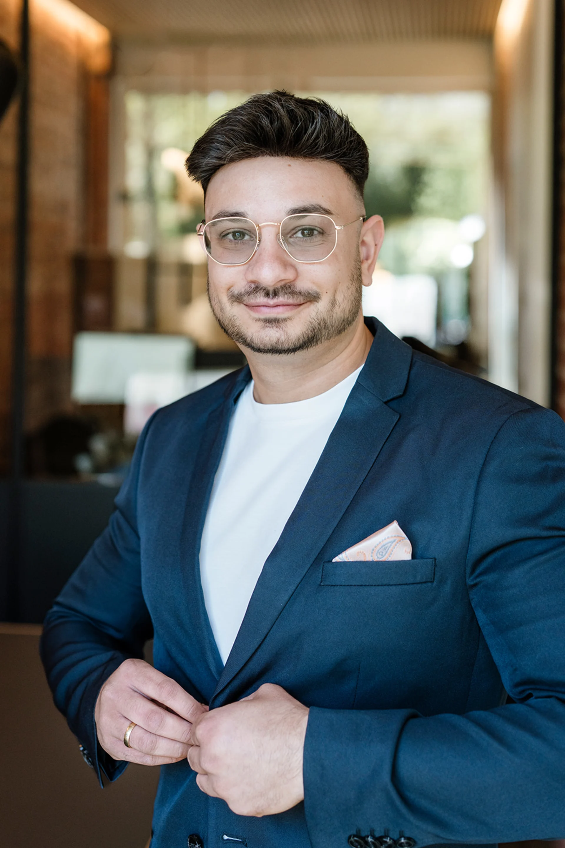 Ein Mann mit Brille und Anzug steht in einem modernen, hellen Raum.