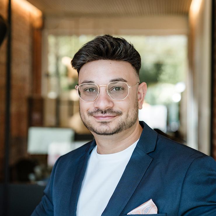 Ein Mann mit Brille und Anzug steht in einem modernen, hellen Raum.