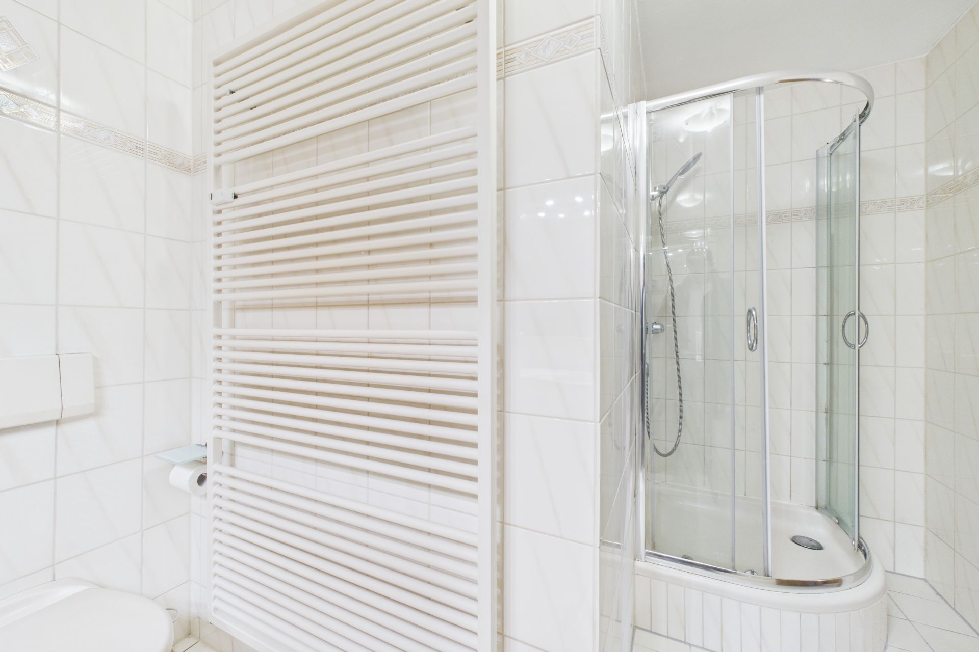 Helles Badezimmer mit Handtuchheizkörper und Eckdusche mit Glaswänden.
