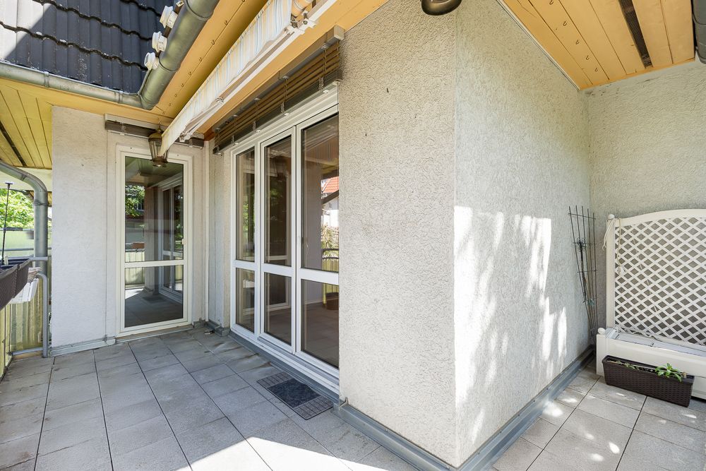 Überdachte Terrasse mit großen Fenstern und einer weißen Bank mit Blumentopf an der Wand.