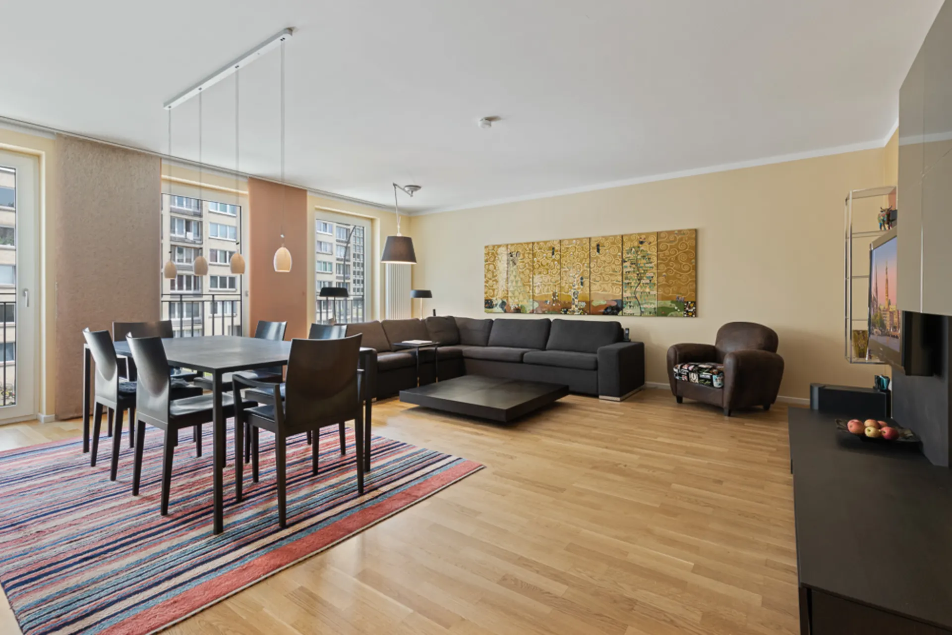 Modernes Wohnzimmer mit Essbereich, großem Sofa, Tisch, Stühlen und buntem Teppich auf Holzboden.