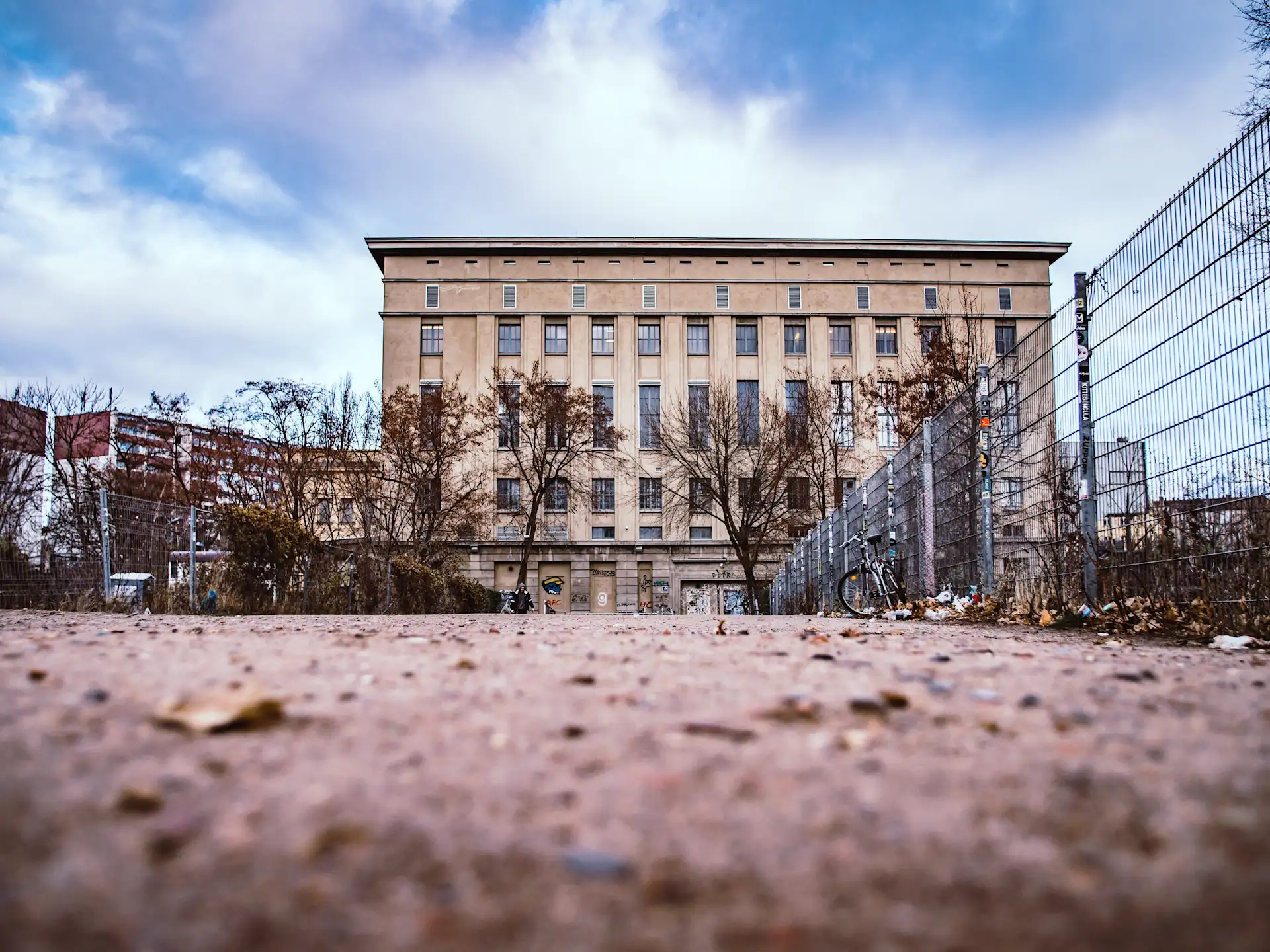 Großes, rechteckiges Gebäude mit vielen Fenstern, umgeben von Zaun und Bäumen.