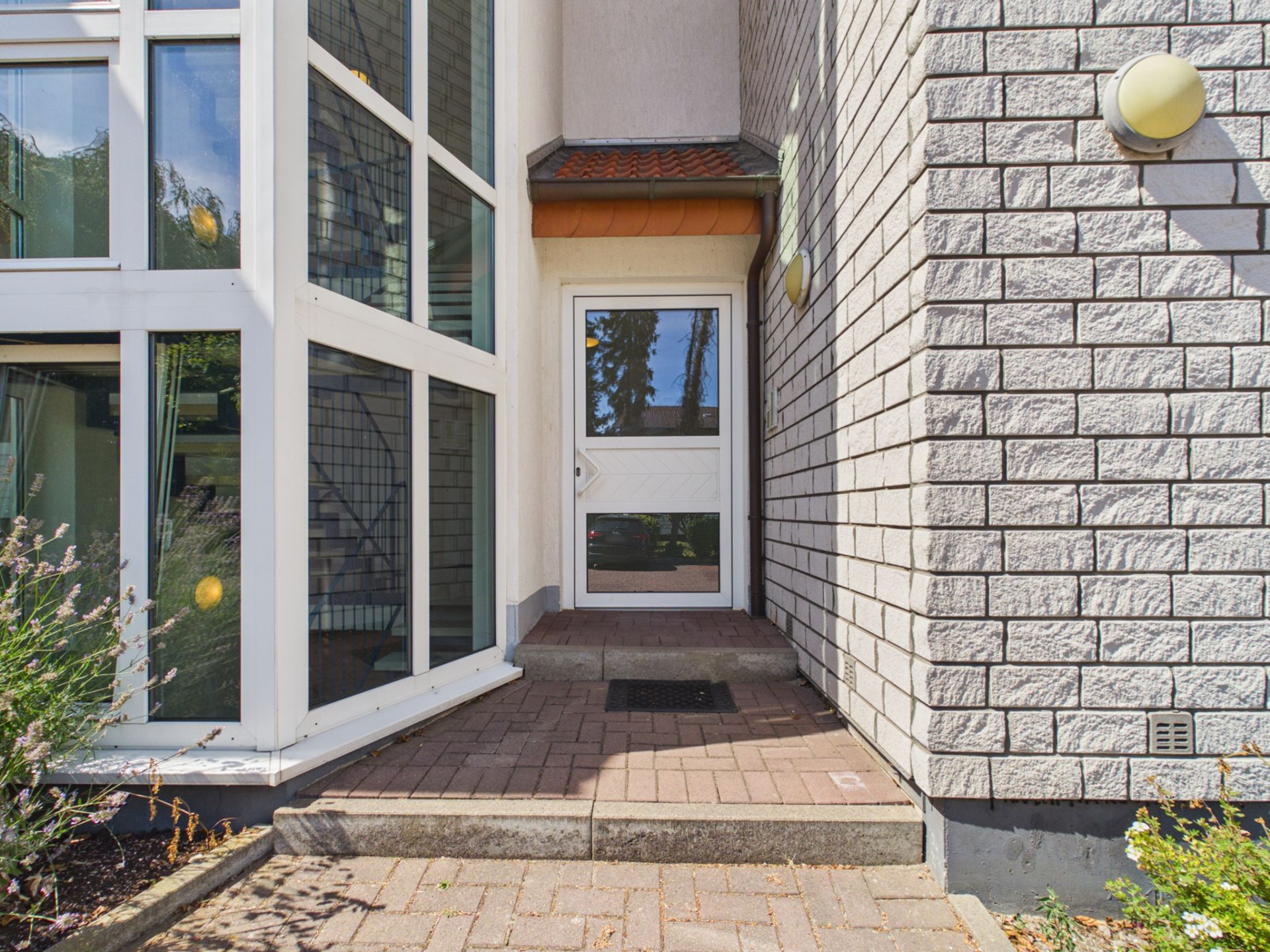 Eingang eines Wohnhauses mit Glasfront und gepflastertem Weg.