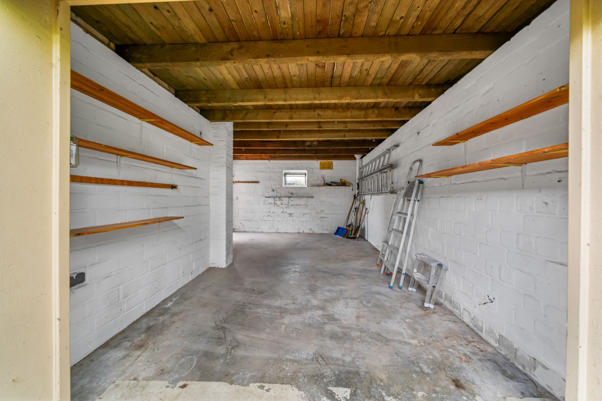 Leere Garage mit weißen Wänden, Regalen, Leitern und Werkzeugen an der Seite.
