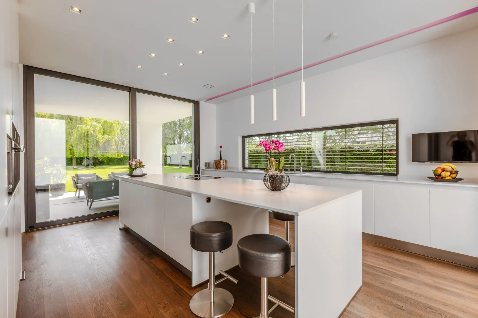 Moderne Küche mit Insel, zwei Hockern und Blick auf Terrasse und Garten.