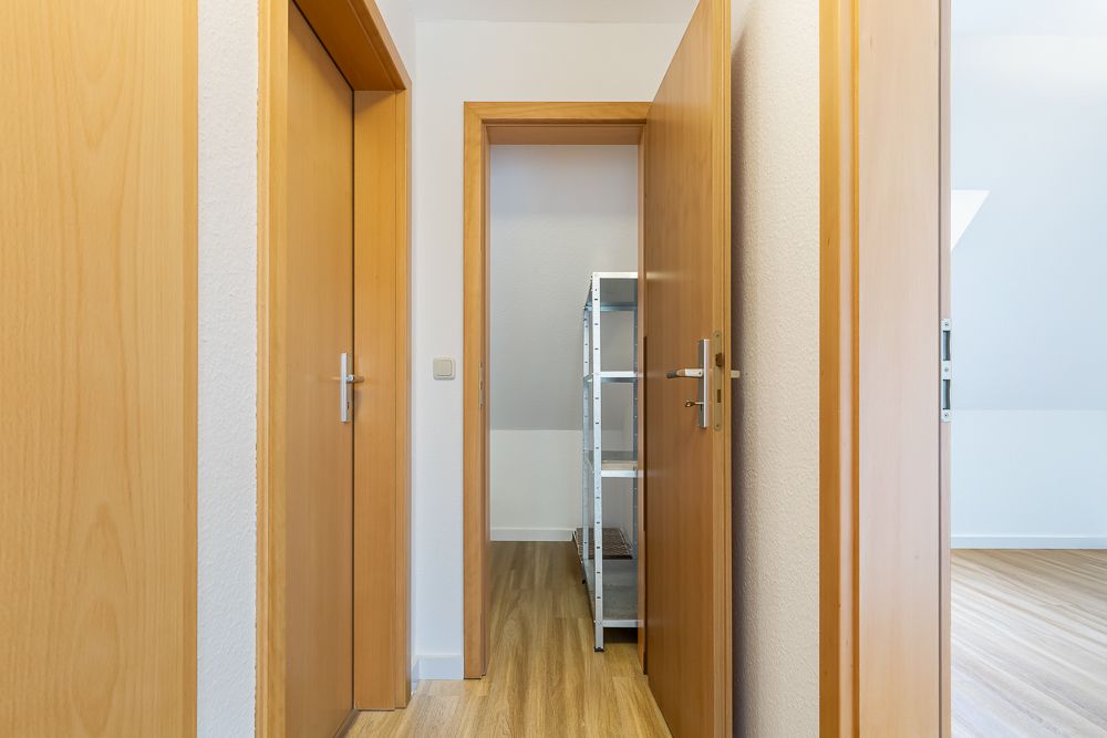 Flur mit Holztüren und Regalen im angrenzenden Raum, heller Holzboden.