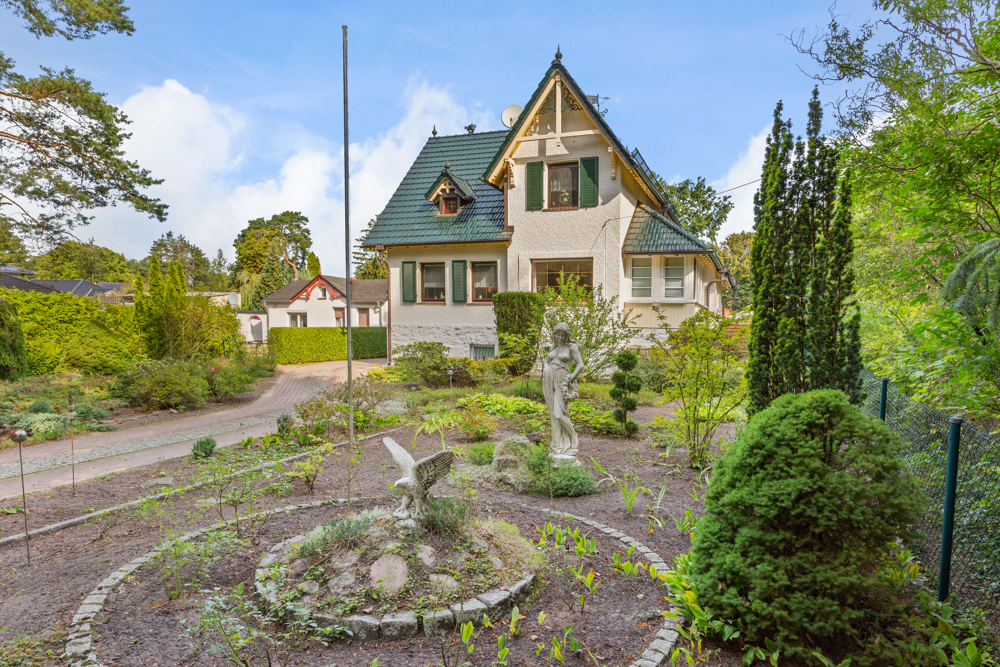 Ein Einfamilienhaus mit grünem Dach und Garten, in dem zwei Statuen zu sehen sind.